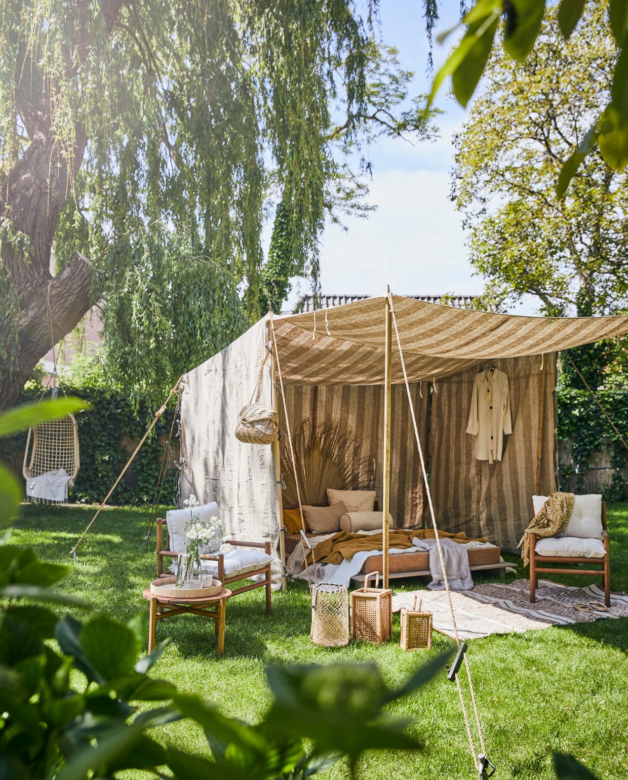 Tent op maat gemaakt, prijs op aanvraag, bed met canvas matras vanaf € 700,-(com-anders.nl). Marantiehouten fauteuil met witte kussens € 149,-, bijzettafel 38x50 cm (hx Ø) € 99,-, lichtbeige vloerkleed, 140x200 cm € 179,- (hm.com). Palmblad € 22,-, wit kussen met franjes 50x50 cm € 55,25, okergeel kussen € 28,-, wit linnen rolkussen € 39,25, gele gedessineerde kimono € 56,50 (madamstoltz.dk). Rotan dienblad € 49,-, glazen kan € 33,50 (weldaad.com). Zandkleurig linnen kussen € 34,95, okergele quilt € 72,- (iblaursen.nl). Rotan hangstoel van HKliving € 199,95, windlicht Ewald van Nordal, groot € 79,95, klein € 59,95 (vtwonen.be). Wit linnen plaid € 304,75, gestreept katoenen plaid € 59,- (nordal.eu). Mok op dienblad € 16,-, rieten tas € 129,-, keramieken kan € 99,- (sukha.nl). Pyjama € 45,99, slippers € 29,99 (zarahome.com). vtwonen 07-2020 | styling Cleo Scheulderman | fotografie Jeroen van der Spek | assistentie Mette Sophie van der Hoek