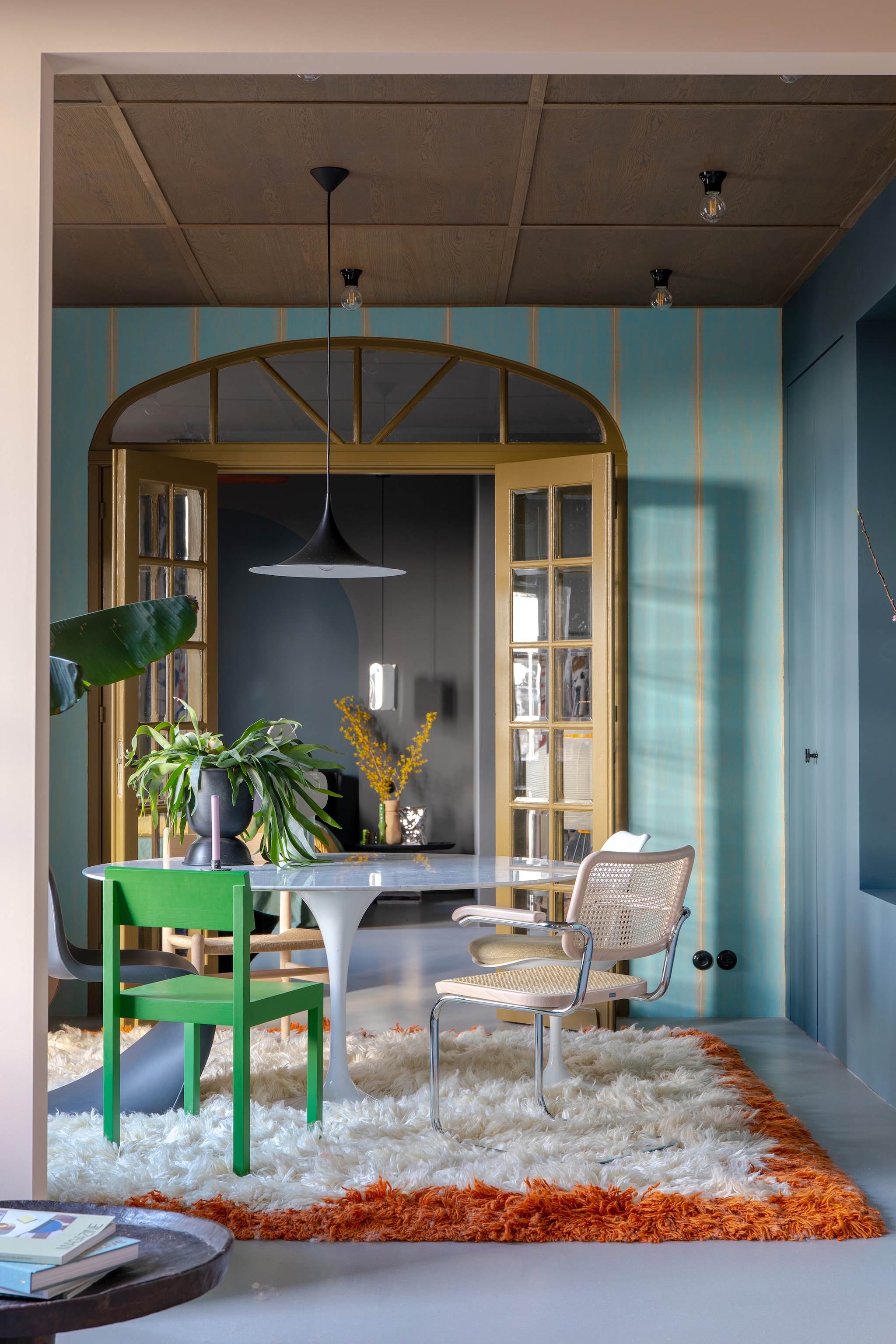 Muurverf 85% Graniet en Puur Marmer van Flexa, behang via Selected Wallpaper. Groene eetkamerstoel Valerie Objects, rotan stoel Thonet, witte stoel Tulip van Eero Saarinen, houten stoel Carl Hansen, zwarte stoel Panton van Vitra, vloerkleed HKliving. Plafond op maat gemaakt door Woodever, hanglamp Gubi, bakelieten plafondlampen Fonq, zilveren hanglamp Hay. Groene kandelaar en chipszak-vaas HKliving, aardewerken vaas MaisonNL, eettafel en en-suitedeuren vintage. Overig onbekend. vtwonen 05-2023 | styling &amp; fotografie Theo-Bert Pot &amp; Jelle van de Schoor