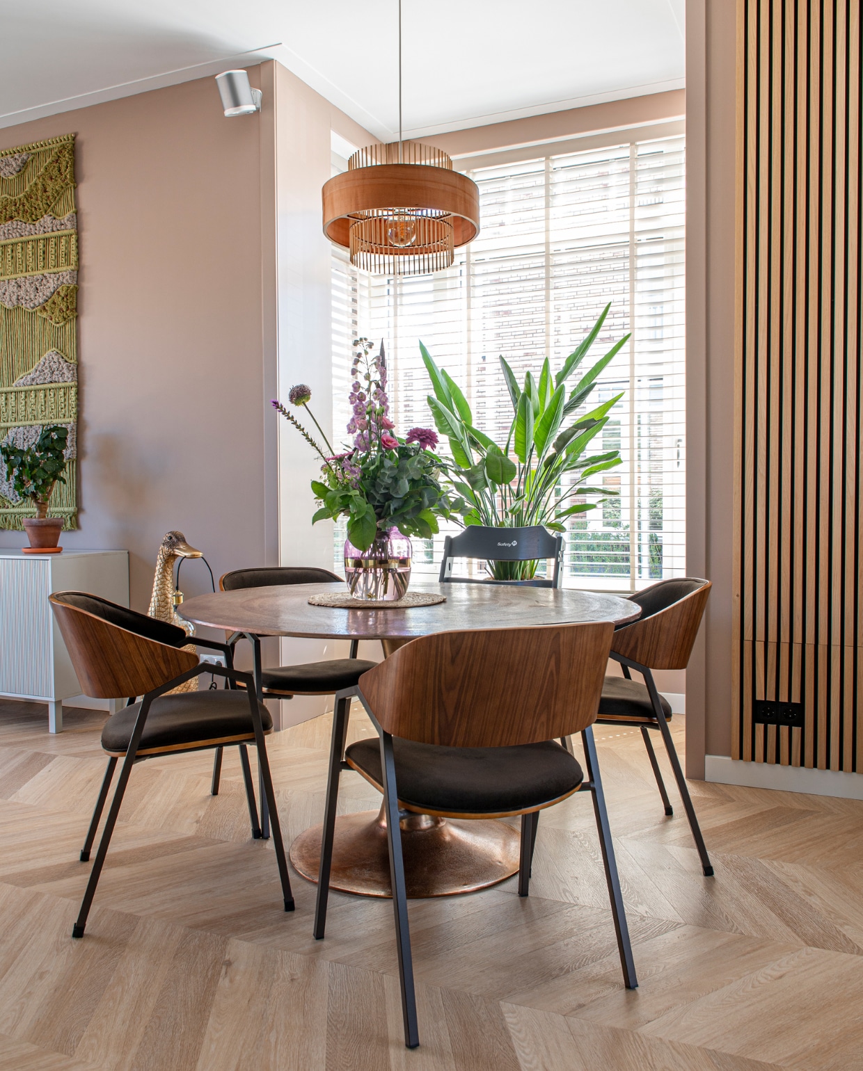 Lamp Studio Melkweg, houten jaloezieën Harmony in taupe van Veneta, tafel Riverdale, stoelen BePureHome.  Wandkleed zelfgemaakt, dressoir Woood, eendlamp Loods 5. Eikenhouten wandpaneel WoodUpp, muurverf Dead Salmon van Farrow &amp; Ball, pvc-vloer in Hongaarse punt Chevron 6541 van Therdex. vtwonen 05-2023 | productie De Binnenkijkers | styling Jeske Weel | fotografie Caroline Coehorst