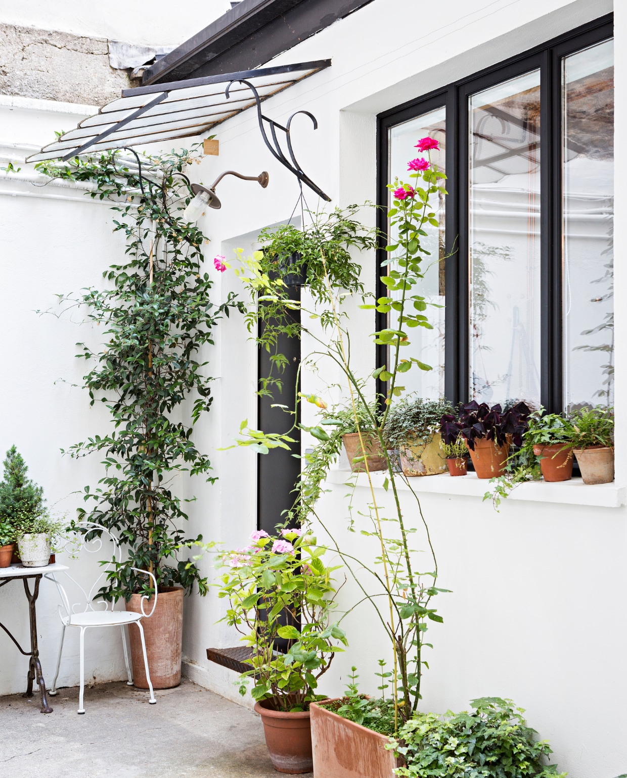 Binnentuin, planten, witte muren, tafel en een witte kruk vtwonen 05-2018 | styling Marie-Maud Levron | fotografie Yann Deret