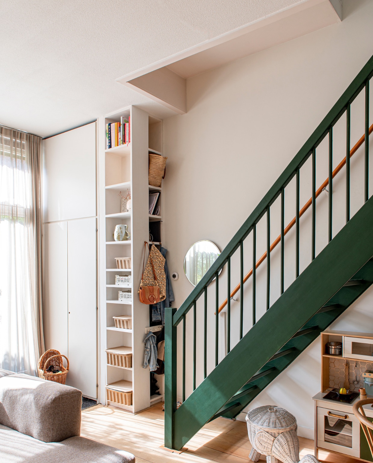 Verfkleur trap Duck Green van Farrow &amp; Ball. Bank Hay. Ronde spiegel en manden in kast Ferm Living. Poppenwagen familiestuk. Overig onbekend. binnenkijk-special vtwonen 131-2023 | fotografie Caroline Coehorst