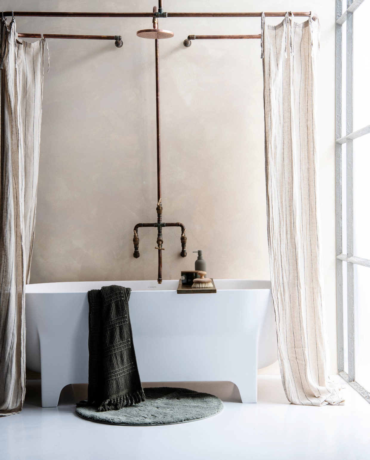 Bad/douche rails van koperen buizen, 164x84x15 cm (lxbxh) € 450,- en koperen douche Elles met badkraan ICM Hotbath en douchekop M100, buisdikte 22 mm x 150 cm hoog € 935,- (Koperen Kranen) Set van 2 beige gestreepte gordijnen met lusjes, 120x250 cm € 49,99 (H&amp;M Home) Ligbad Thorgan, 171x75,5x60 cm € 2575,- (Detremmerie) Messing badbrug, p.o.a. (Julius Baller) Houten massage badborstel € 26,05 (zangra.be) Matgrijze zeepdispenser € 23,65 (Ton Scholten) Keramieken geurkaarspot met deksel € 14,95, donkergroene badmat Elwin € 10,- en saliegroene badmat Gabriel € 25,- (alles Loods 5 goods) Muurverf Limewash paint, kleur Dream, per liter € 30,- (Bauwerk Colour) vtverbouwen badkamer 02 | productie en styling Marit Saladini | fotografie Louis Lemaire