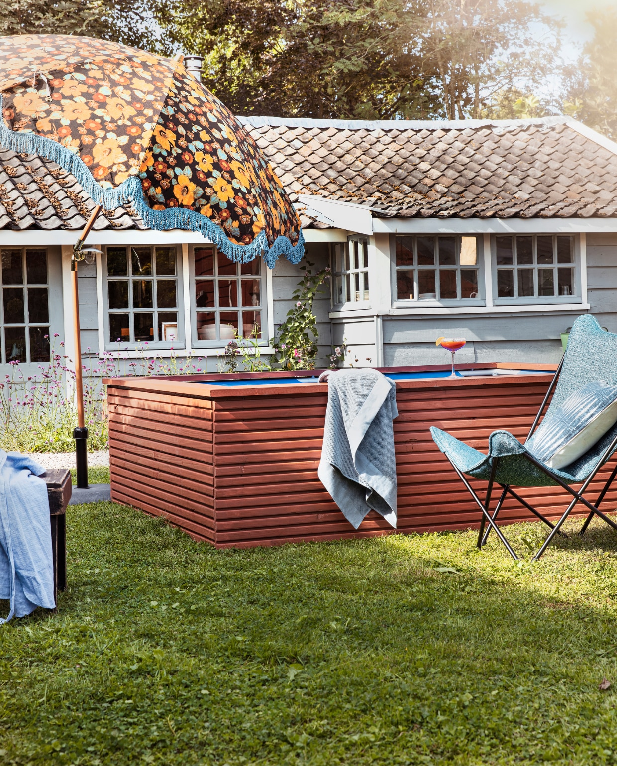 Zwembadombouw geschilderd met Traditional Paint Dry Terra, per liter € 59,40 (pure-original.nl). Loungestoel Sphinx van Lafuma in Cobalt, staal en Sunbrella-stof € 284,99, parasol Floral Energy van HKliving € 369,- (vtwonen.be)/shop). Badlaken Basic € 14,99 (hm.com). Blauwe overhemdjurk € 39,99 (zara.com). Kussen tie-dye € 19,95 (loods5.nl). Overig privébezit. vtwonen tuin special 08 | productie Corrien Flohil | styling Moniek Visser | uitvoering zwembadombouw Studio Milo