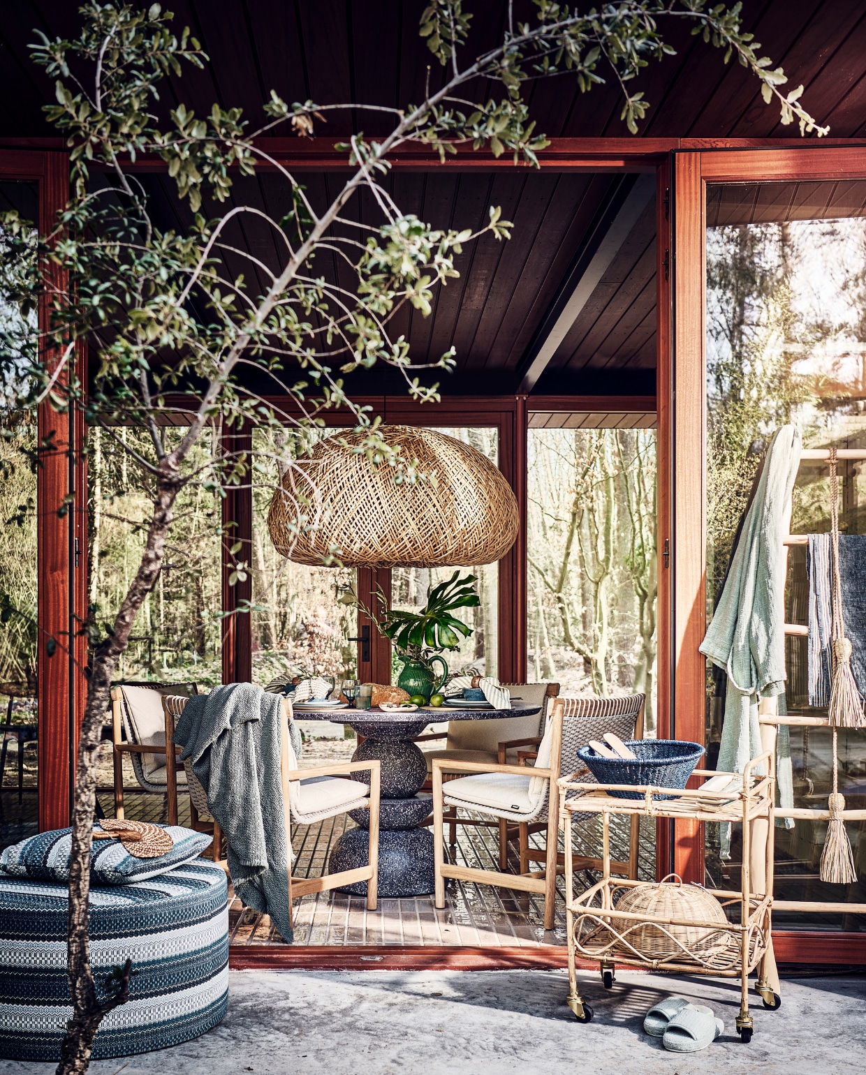 Tafel voor binnen en buiten, 130 cm (Ø) vanaf € 2495,- (lanena-home.com). Duurzaam teakhouten stoelen, per stuk € 1675,-, poef met print € 949,-, kussen met print € 169,- (dacks.nl). Badjas € 285,-, blauwe plaid € 325,- (brechtmurreatelier.nl).  Rotan lamp Nido, 115x110x62 cm (lxbxh) € 1590,-, waaier € 36,-, bamboe trolley, 55x44x80 cm (lxbxh) € 275,-, olijfhouten ladder € 285,-, palmblad schaal op trolley uit Burkina Faso € 19,-, blauw gerecycled waterglas Bubbel € 11,-, blauw gerecycled wijnglas € 15,-, langwerpig bord van Wonki Ware € 14,-, slinger van gras € 33,-, hanglamp € 343,- (couleurlocale.eu). Kan € 59,-, gestreepte theedoek aan ladder € 8,95, bakjes in vorm van vis op trolley € 17,95 (maisonnl.com). Bestek, 16-delig € 89,99, afdekmand in trolley, prijs op aanvraag, servetring, set van 2 € 7,99, placemat, set van 2 € 4,99 (hm.com). Slabestek € 19,95 (urbannatureculture.com). Slippers € 25,99, servet € 6,99 (zarahome.com). Blauw servies Matera van Leonardo, 18-delig € 140,99 (vtwonen.be/shop). Takken, prijs op aanvraag (plantje.nl). vtwonen 06-2023 | styling Liza Wassenaar | fotografie Sjoerd Eickmans