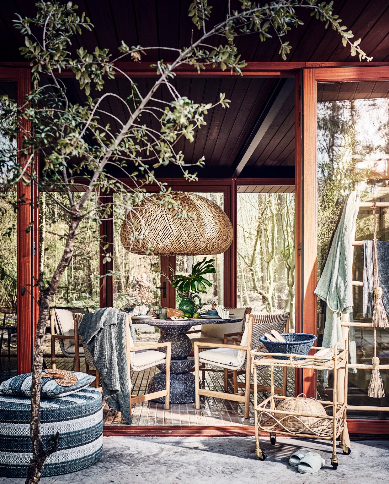 Tafel voor binnen en buiten, 130 cm (Ø) vanaf € 2495,- (lanena-home.com). Duurzaam teakhouten stoelen, per stuk € 1675,-, poef met print € 949,-, kussen met print € 169,- (dacks.nl). Badjas € 285,-, blauwe plaid € 325,- (brechtmurreatelier.nl).  Rotan lamp Nido, 115x110x62 cm (lxbxh) € 1590,-, waaier € 36,-, bamboe trolley, 55x44x80 cm (lxbxh) € 275,-, olijfhouten ladder € 285,-, palmblad schaal op trolley uit Burkina Faso € 19,-, blauw gerecycled waterglas Bubbel € 11,-, blauw gerecycled wijnglas € 15,-, langwerpig bord van Wonki Ware € 14,-, slinger van gras € 33,-, hanglamp € 343,- (couleurlocale.eu). Kan € 59,-, gestreepte theedoek aan ladder € 8,95, bakjes in vorm van vis op trolley € 17,95 (maisonnl.com). Bestek, 16-delig € 89,99, afdekmand in trolley, prijs op aanvraag, servetring, set van 2 € 7,99, placemat, set van 2 € 4,99 (hm.com). Slabestek € 19,95 (urbannatureculture.com). Slippers € 25,99, servet € 6,99 (zarahome.com). Blauw servies Matera van Leonardo, 18-delig € 140,99 (vtwonen.nl/shop). Takken, prijs op aanvraag (plantje.nl). vtwonen 06-2023 | styling Liza Wassenaar | fotografie Sjoerd Eickmans