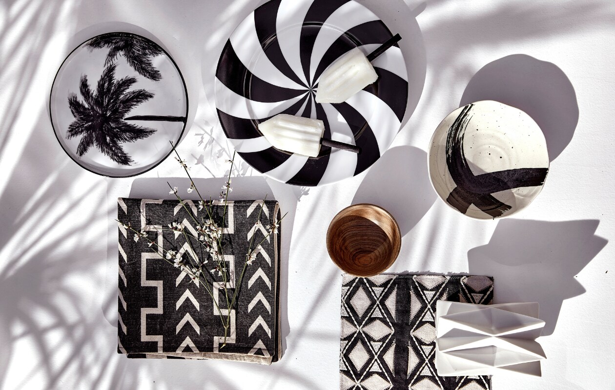 Kussenhoes € 24,95 (mrsbloom.nl). Schaal met kruis, set van 4 € 33,56, ontbijtbord met palmboom, 22 cm (Ø) € 9,95 (hkliving.com). Stof Sojourn-Domino van Pollack, per meter € 246,- (ateliersem.nl). Geometrische kandelaar, 10x14 cm (Øxh) € 17,95, bord met zwart-witte strepen Hypnotise Mesmerise van House Of Rym, 25 cm (Ø) € 22,50 (livvlifestyle.nl). Houten kom € 12,95 (householdhardware.nl). vtwonen 06-2023 | styling Kim Timmerman | fotografie Peggy Janssen