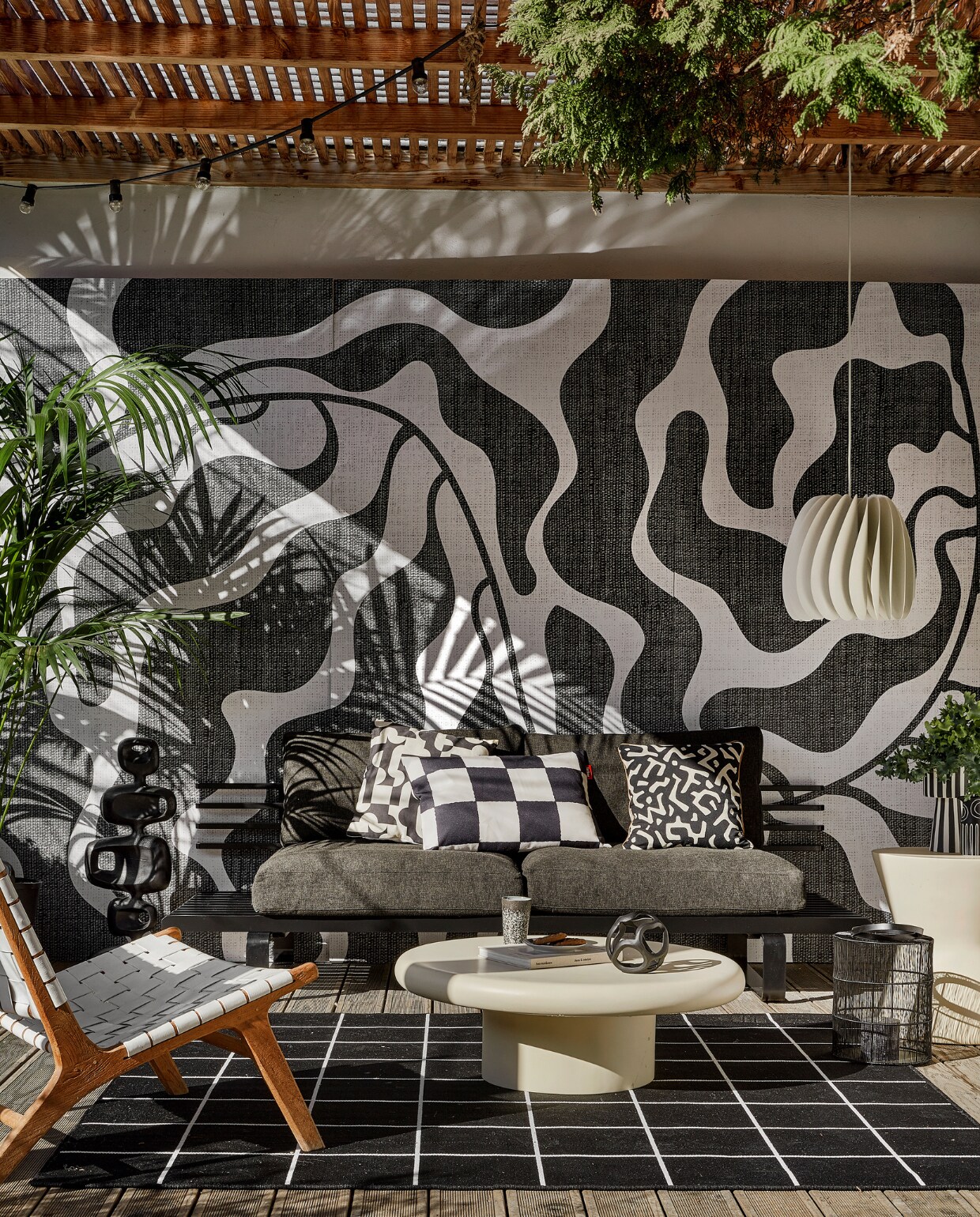 Behang River black &amp; white van Wrap the Wall, per m2 € 150,-, minimale afname 4 m2 (behangfabriek.nl). Zwarte aluminium buitenbank € 1339,80, antraciet tuinkussens, per set € 675,75, zwarte aluminium sculptuur € 295,-, mok 70s, per 2 € 19,99 (hkliving.com). Buitenvloerkleed Svallerup, 200x200 cm € 79,95, hanglamp Skymningen € 79,95 (ikea). Ivoorkleurige polyester bijzettafel, 85x30 cm (Øxh) € 599,-, bijzettafel Pot-Table in Ivory-Slim € 395,- (householdhardware.nl). Zwart-wit kussen Cutro € 10,- (kwantum.nl). Zwart-wit geblokt kussen King Pillow € 55,- (fatboy.com). Kussen Nara € 59,90 (ateliersem.nl). Zwart-wit gestreepte pot van Oyoy € 69,95, aardewerken vaas Troy van Bloomingville € 12,95 (livvlifestyle.nl). Zwart aluminium bolvormig ornament € 31,95, lantaarn € 96,95 (ptmd.nl). Fauteuil met gevlochten zitting privébezit, soortgelijke bij Kave Home (kavehome.com). vtwonen 06-2023 | styling Kim Timmerman | fotografie Peggy Janssen