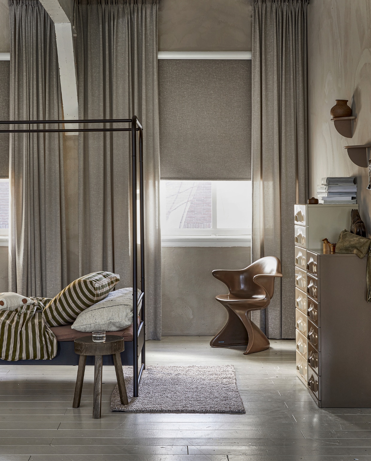 Lichtdoorlatend gordijn op maat, met dubbele plooi in stof Grain (1772) kleur Kiezel vanaf € 26,99 per strekkende meter. Verduisterend rolgordijn op maat in kleur bruin slub (18007) vanaf € 110,50. M.m.v.: hkliving.nl (eetkamerstoel Sedia moka, retro ladenkasten), hm.com (vloerkleed, wandplanken, houten doosje), beddinghouse.nl (dekbedovertrek Pyjamas), basiclabel.nl (bijzettafel Sef, bedframe Bunk), rawmaterials.eu (beeldje Nandi XL, bruine vaas), pure-original.com (kalk muurverf Fresco in kleur Canvas), vtwonen.be/shop (kussen met stippen van vtwonen, lakverf vloer kleur Flax). vtwonen 06-2023 | productie Tanja Saarberg | styling Marit Saladini Platjouw | fotografie Peggy Janssen