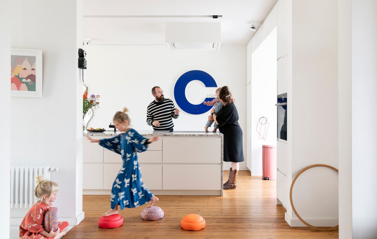 De keuken is een ontwerp van Isabelle en een architect. Print Swantje Hinrichsen, letter C tweedehands, spiegel Ferm Living, roze vuilnisbak Brabantia. Stapelstenen Stapelstein via Blabloom. Aan de wand onderzetter Trivets van Muller Van Severen, kattenklok Kit-Cat Clock. Hoepel kringloopwinkel, keukenblad Terrazzo van Bomarbre, apparatuur Bosch. Vloer (originele) grenen planken met kleurloze olie. vtwonen 06-2023 | styling &amp; fotografie Jonah Samyn