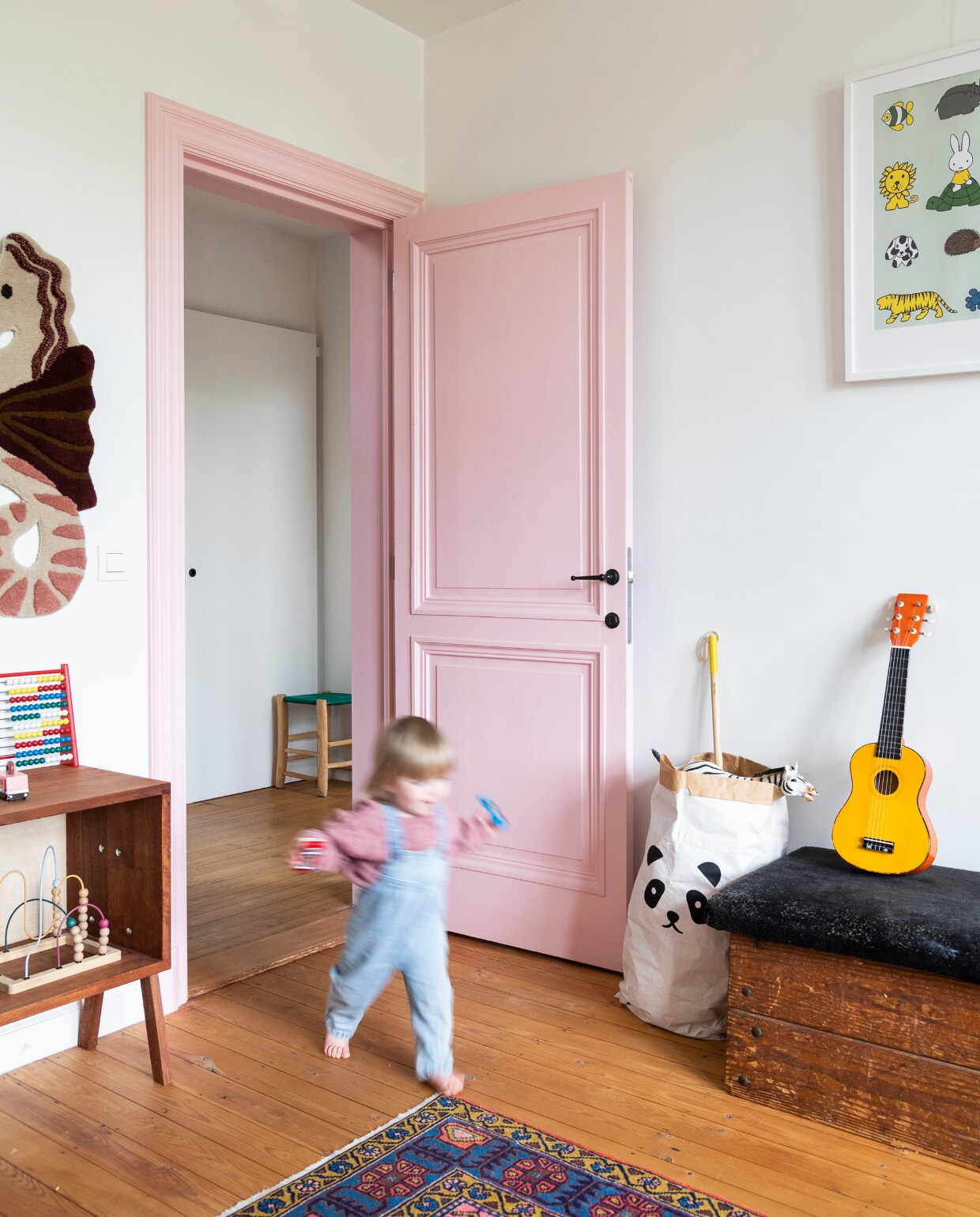 Poster Nijntje, papieren zak Kolor, gitaar kringloopwinkel. Houten plint vintage, vloerkleed Ikea, kastje op maat Hannemans. Wanddecoratie zeepaard Ferm Living. Verf deur Levis, kleurcode onbekend. Vintage turnkast met suède kussen, telraam in kast Zara Home. Vloer (originele) grenen planken met kleurloze olie. vtwonen 06-2023 | styling &amp; fotografie Jonah Samyn