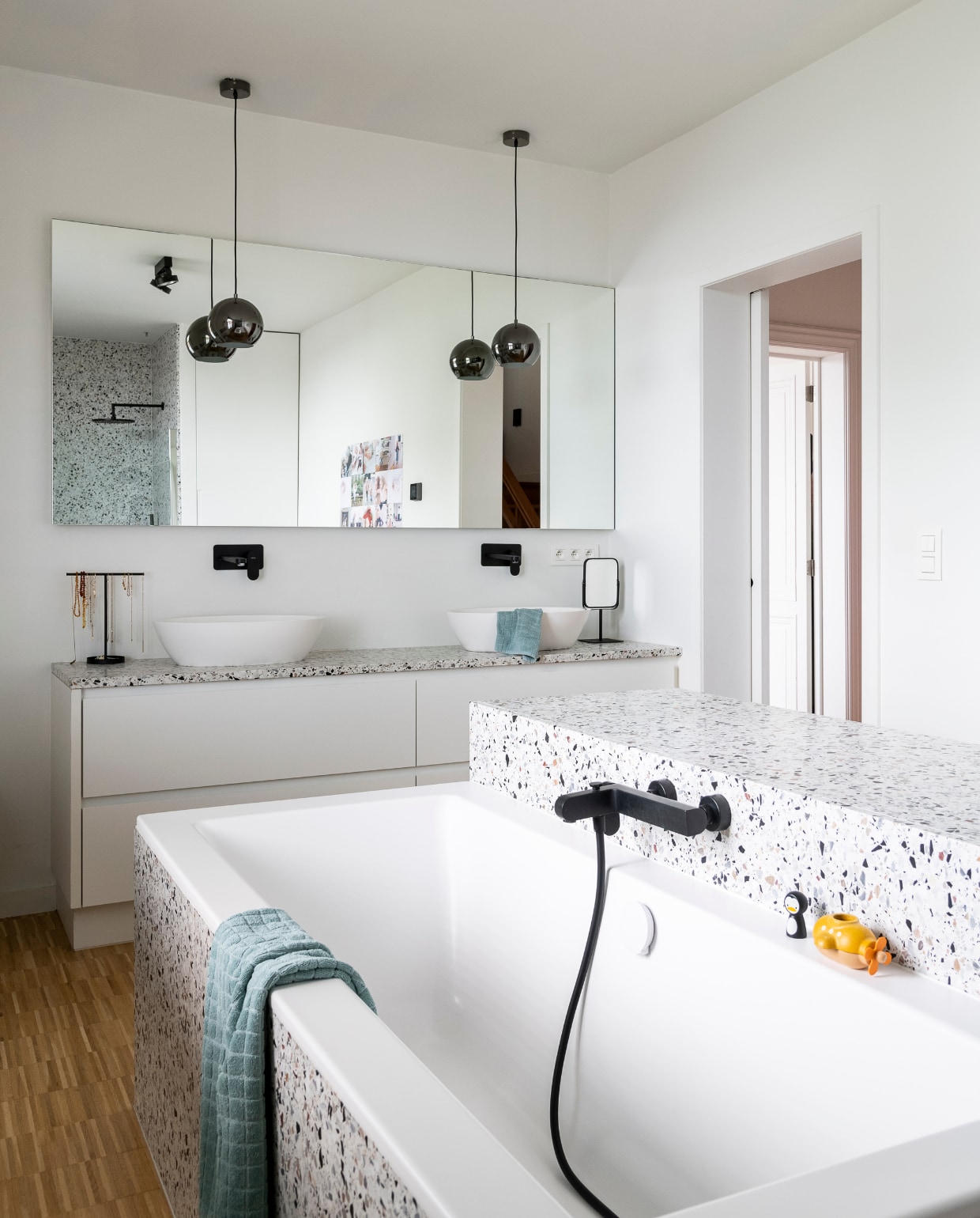 Badkamer op maat laten maken, materiaal Terrazzo van Bomarbre, bad Villeroy &amp; Boch, wastafels Senzo Xonyx van Desco, kranen Nobili. Sieradenhouder H&amp;M, handdoeken Ikea, spiegel op voet Aquanova. Speelgoed op badrand Janod, wanddecoratie IXXI. Vloer lamel op kant in eik met kleurloze vernis. Lampen onbekend. vtwonen 06-2023 | styling &amp; fotografie Jonah Samyn