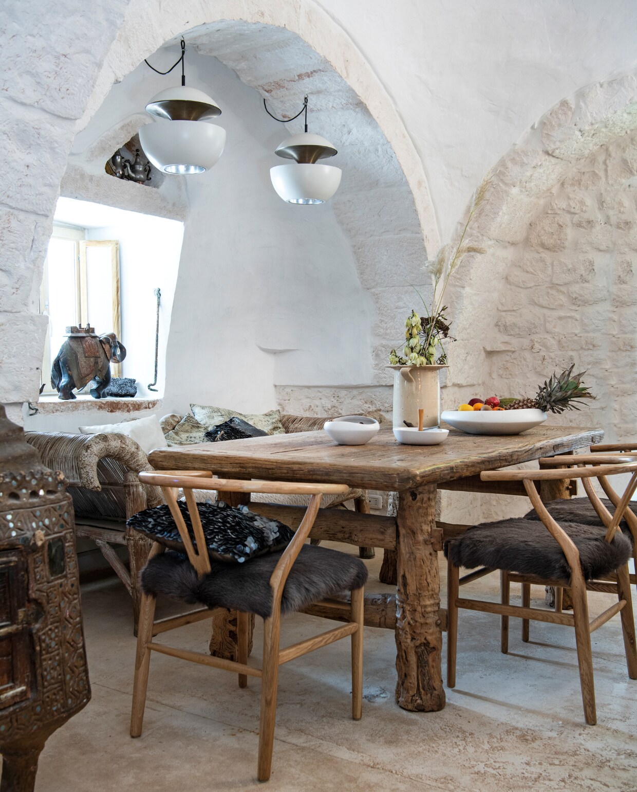 Chinese iepen-houten eettafel. Wishbone-stoelen Gert Snel Interiors. Zwart paillettenkussen PTMD. Palmhouten loungebank en oude struisvogelei-broedmachine (links) uit Indonesië. Retro hanglampen Raak. Aardewerken vaas antiekmarkt Ostuni. Fruitschaal Now’s Home. Schaaltje met houten handvat Yong. In de nis: twee Toeareg-theepotjes. Overig onbekend. vtwonen special binnenkijken 06-2022 | productie Insidehomepage | styling Marit Saladini Platjouw | fotografie Louis Lemaire