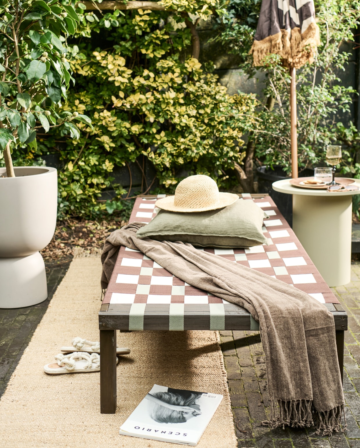 Grenenhouten frame daybed, 200x70x31,5-77 cm (lxbxh) € 67,99 (vidaxl.nl). Parasol van HKliving € 369,- (bijenkorf.nl). Grijze bloempot van Elho € 145,-, bijzettafel van HKliving € 249,- (vtwonen.nl/shop). Plaid € 24,99, kussen € 12,99, juten vloerkleed € 42,99 (hmhome.nl). Glazen karaf € 17,99, houten dienblad € 17,99, glas € 5,99 (zarahome.com). Overig privébezit. vtwonen 06-2023 | styling en uitvoering Sanne Ketelaar | fotografie Sjoerd Eickmans
