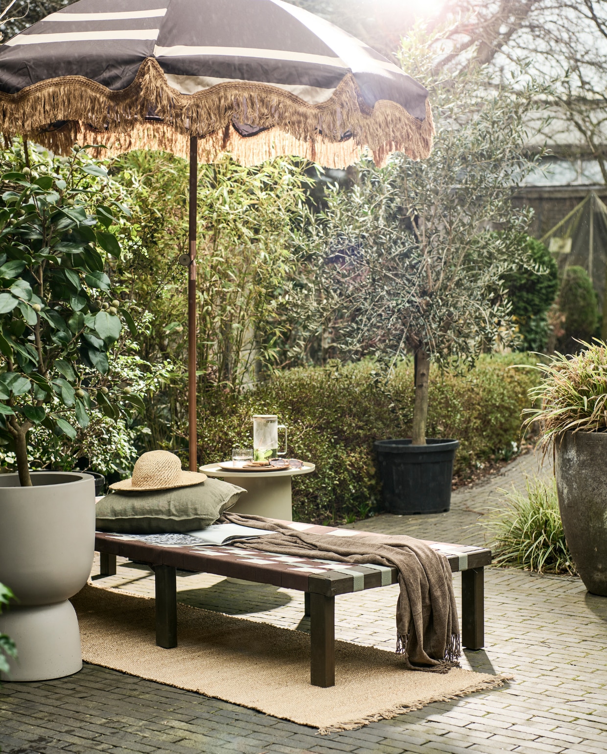 Grenenhouten frame daybed, 200x70x31,5-77 cm (lxbxh) € 67,99 (vidaxl.nl). Parasol van HKliving € 369,- (bijenkorf.nl). Grijze bloempot van Elho € 145,-, bijzettafel van HKliving € 249,- (vtwonen.be/shop). Plaid € 24,99, kussen € 12,99, juten vloerkleed € 42,99 (hmhome.nl). Glazen karaf € 17,99, houten dienblad € 17,99, glas € 5,99 (zarahome.com). Overig privébezit. vtwonen 06-2023 | styling en uitvoering Sanne Ketelaar | fotografie Sjoerd Eickmans