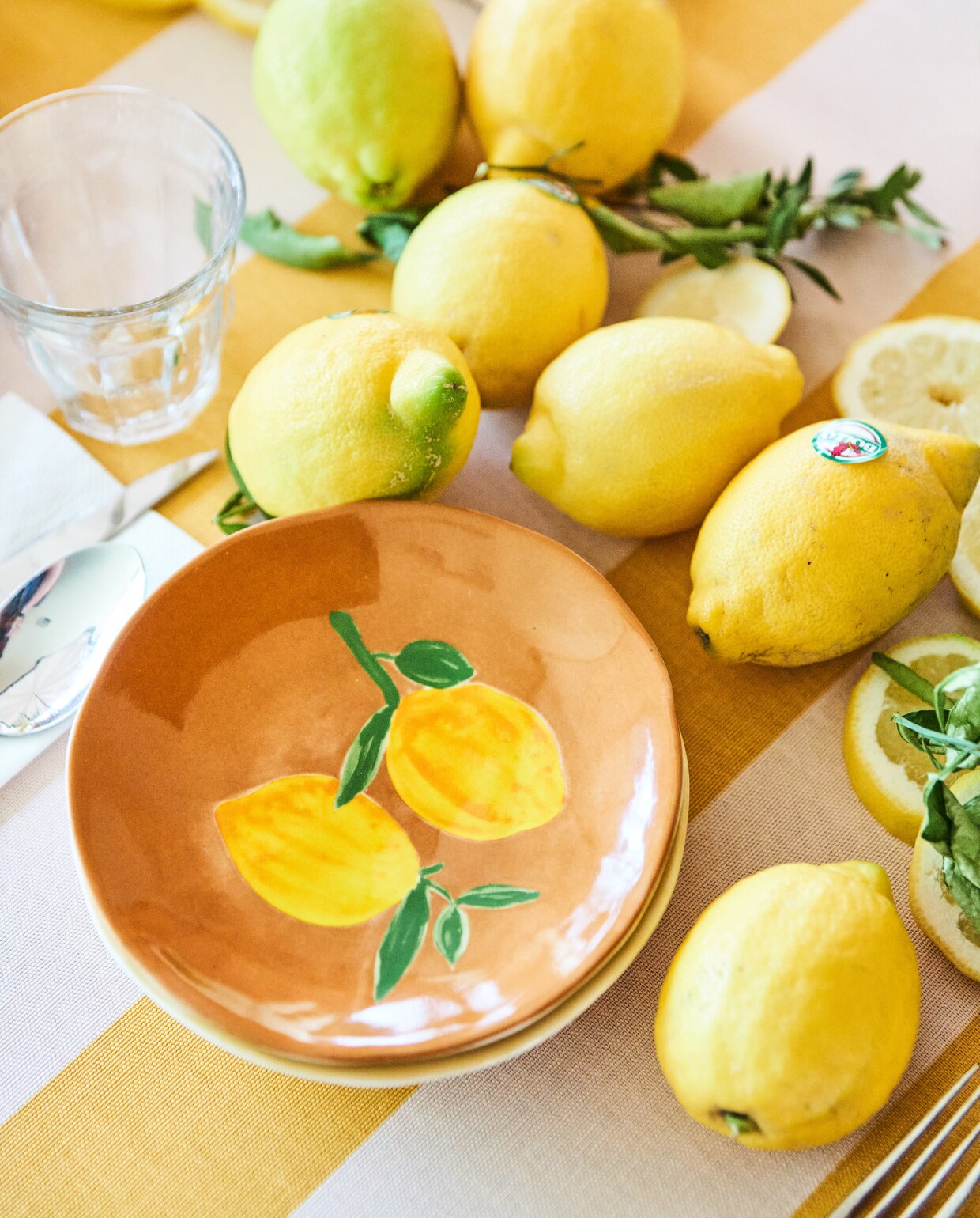 Bord Lemon van &amp;Klevering, 16 cm (Ø), set van 4 (debijenkorf.nl). Tafelkleed met streepdessin van Sylke gordijnstof, 150 cm breed (kwantum.nl). Glazen, karaffen en bestek, privébezit restaurant dudok.nl. vtwonen 07-2023 | styling Marit Saladini | fotografie Bart Brussee