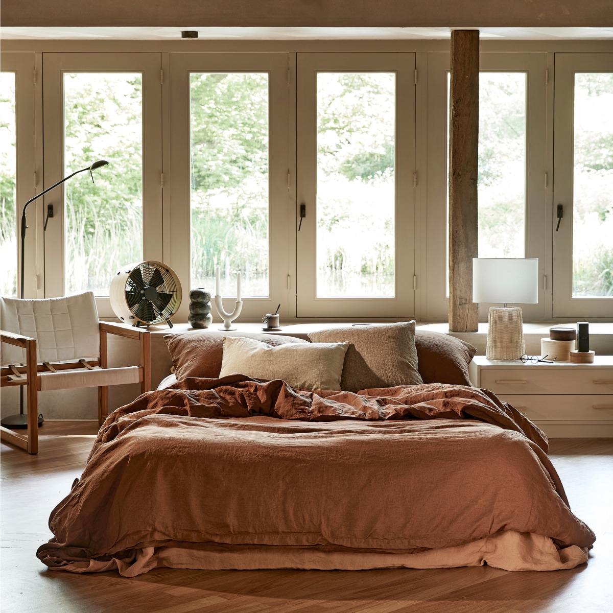 Linnen dekbedovertrek van het duurzame merk Yumeko in kleur Almond Brown, 240x220 cm, daaronder linnen dekbedovertrek in kleur Terracotta, 240x220 cm (yumeko.nl). Naturel linnen kussen, 40x60 cm, linnen kussens, 40x60 cm (bymolle.com). Safaristoel, hout met zitting van stof en leren riempjes ontworpen door Karin Mobring (dezaakvansjaak.nl). Vintage ladekastje geschilderd met duurzame verf in kleur 03 Nougat van L_Authentique (lauthentique.nl) (hetgoed.nl). Grenenhouten handgrepen Thom (gamma.nl). Vintage leeslamp op voet, geschilderd met duurzame verf in de kleur 48 Aarde van L_Authentique (lauthentique.nl), vintage houten doosjes (hetgoed.nl). Bamboe ventilator (bymolle.com). Duurzame rotan tafellamp Kimjit, 51x33 cm (hx_), witte ecomix kandelaar Urban Nature Culture, 18 cm (h), zwart-witte kop en schotel Inlay van Ferm Living (vtwonen.nl). Zwarte aardewerken vaas Hang, 22x11 cm (hx_), geweven vloerkleed Hetan van hennep, 120x180 cm (homata.fr). vtwonen 07-2022 | styling Marlies Does | fotografie Peggy Janssen