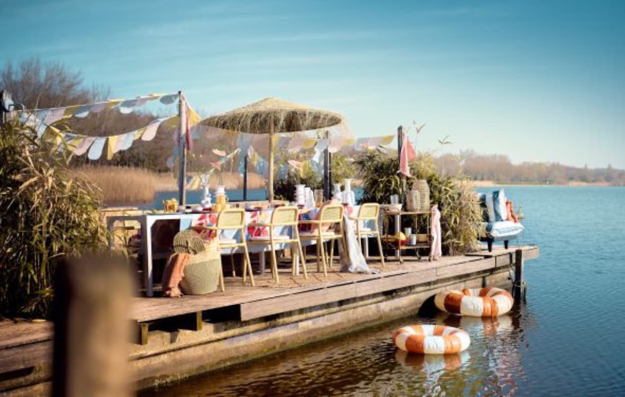 Vlaggen gemaakt van oude dekbedovertrekken, lange tafel gemaakt door Combitex, stalen poten en houten bovenblad, prijs op aanvraag (com-anders.nl). Stoelen Toní Armchair van Fatboy, set van 2, waterglazen Pure van Serax, 0,2 liter, set van 4, karaf Pure van Serax op trolley, 1,2 liter, blauwe glazen Terres de Rêves van Serax in trolley, 0,34 liter, blauwe borden Pure van Serax, 9-delig, okerkleurige bijzettafel Filippo van Serax, 40x46 cm (Øxh), witte vazen Billy van Serax, 27 cm (h), 30 cm (h), 37 cm (h), 31 cm (h), waterdispenser van Serax, 10 liter, zilverkleurig bestek Base van Serax, 24-delig, blauw-wit gestreepte fauteuils Paletti Seat van Fatboy, grote rotan grote lantaarn Ferdi van Bloomingville, (vtwonen.be/shop). Zwemband Celine van Petites Pommes, zwemband Sally van Petites Pommes, bamboe trolley, waaier in tas maat M, tas Capazo Maya L, gele karaf Amber, gevlochten parasol uit Marokko, 200x240 cm (Øxh) (couleurlocale.eu). Roze ontbijtborden, 17 cm (Ø), set van 12, oranje handdoek, oranje glazen karaf, gele theeglazen, set van 4 (sissy-boy.com). Blauw-wit geblokt wollen plaid, roze linnen kussen op bank, 40x60 cm, geel-wit gestreept kussen, 50x50 cm, oranje-wit geruit kussen, 50x50 cm, blauwe kommen, roze-witte theedoeken geknoopt als vlaggen, set van 3, klein zeegras windlicht op trolley, lopers, blauw-wit tafelkleed, 140x180 cm, roze linnen servet, 45x45 cm, set van 2, keramieken vergiet op trolley (hm.com). Mand met citroenen (dekringloper.nl). Geel-wit gestreepte stoelkussens (fatboy.com). Donkerroze schaal in trolley, prijs op aanvraag (zarahome.com). Takken, prijs op aanvraag (waterdrinker.nl). Overig privébezit. vtwonen 07-2023 | styling Liza Wassenaar | fotografie Sjoerd Eickmans