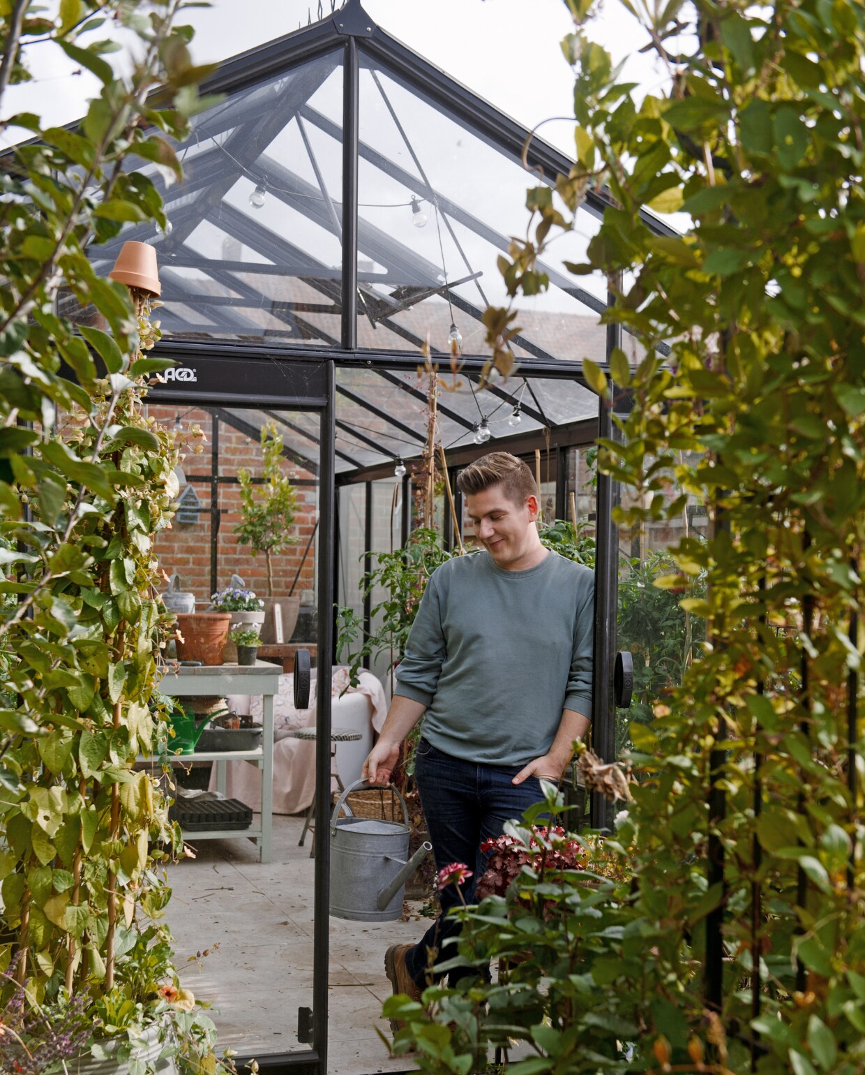 De tuin gezien vanaf het terras, met op de achtergrond de zelfgebouwde kweekkas en schuur, met daarvoor een catalpa (trompetboom). Tegen de kas groeit blauweregen (wisteria) en clematis. De bomen op de voorgrond zijn moerbeibomen. Eromheen groeien onder meer buxusplanten, korenbloemen, sieruien, Siberische irissen en persicaria (duizendknoop). vtwonen 2022-special TUIN 5 | Bk 4 | Styling Ilona Jongepier | Fotografie Brenda van Leeuwen