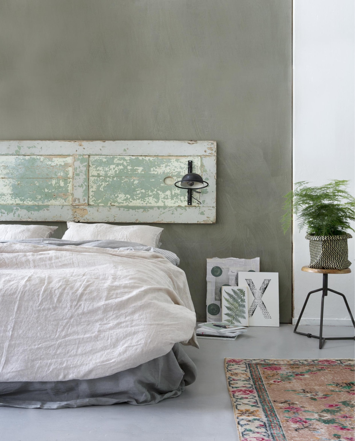 Deur (). Verf op de muur: Olive van Bauwerk lime paint ().  (Bodilson). Dekbedovertrek zwart-wit  (Ikea). over voeteneinde matras Aina (Ikea). Linnen dekbed- overtrek naturel, linnen kussenhoezen naturel (). Vloerkleed (). Kunstwerken tegen muur: krantencollage op hout van Marjon Hoogervorst, letter X van Marjon Hoogervorst (). Botanische afbeelding op hout (). (Basiclabel). Magga (Ikea). vtwonen 08-2015 | fotografie Anouk de Kleermaeker | styling Leonie Mooren