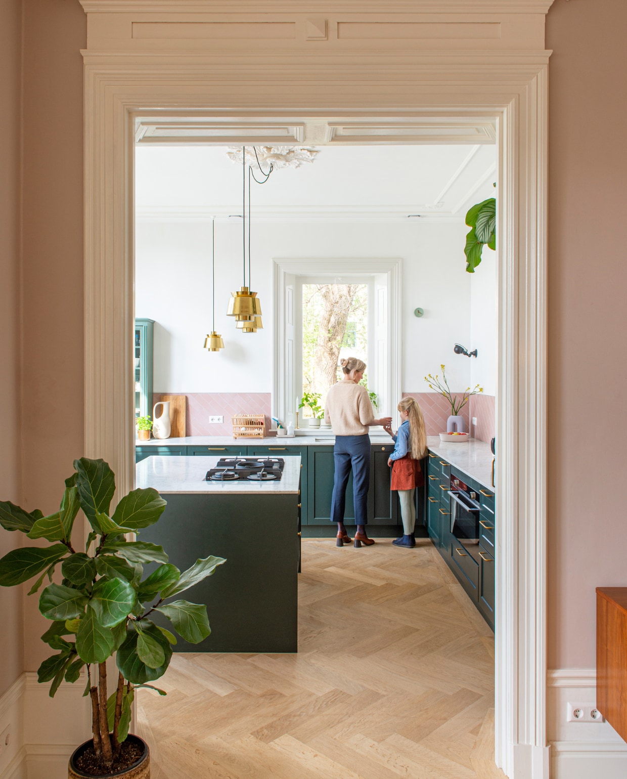Keukenfronten Noremax, geverfd in Studio Green van Farrow &amp; Ball. Tegels Tegelstore. Hanglampen &amp;Tradition. Wandlampen Jieldé. Gieter Ferm Living. Afdruiprek Dille &amp; Kamille. Klok en roze fruitschaal Studio Harm en Elke. Paarse vaas H&amp;M Home. vtwonen special binnenkijken 03-2023 | productie De Binnenkijkers | styling Jeske Weel  fotografie Caroline Coehorst
