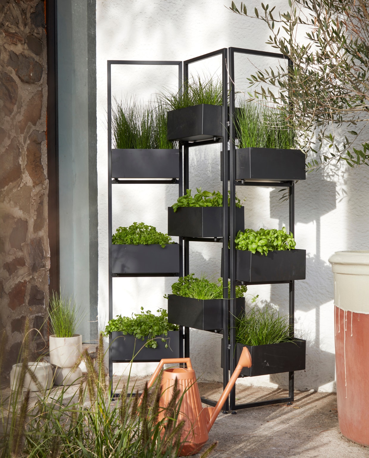 Zwart plantenscherm Nando, 120x25x178 cm (bxdxh) (intratuin.nl). Lage grijze pot (kringloop). Hoge lichtgrijze cementen pot Ajonu van Nordal, 19x28 cm (Øxh) (byflou.com). Terracotta gieter, 47x25x39 cm (lxbxh) (karwei.nl). vtwonen special tuin 7-2023 | Fotografie Peggy Janssen | Styling Kelly van Gendt
