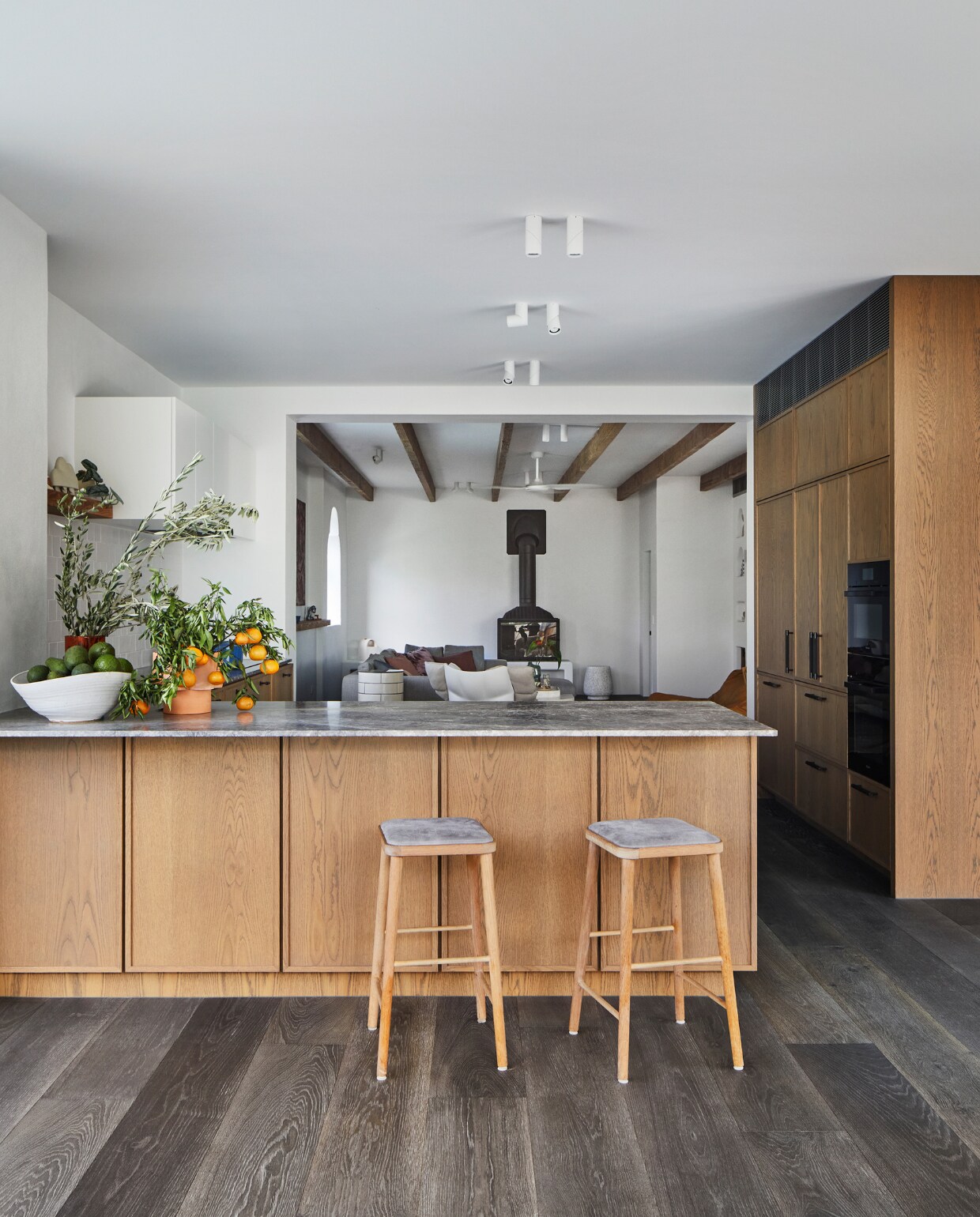 Op maat gemaakte keuken van Amerikaans eiken met beits van Whittle Wax in tint Waterbuck grey, keukenblad Portsea Grey van CDK Stone, hand-grepen Spiggy van Buster + Punch. Barkrukken Hastings Stool van het Australische Green Cathedral Furniture. Oven Miele. Vloer Royal Oak. Plafondlampen Axis Unios. Keramiek Elke Lucas en Clay Canoe. Op de achtergrond: haard van Cheminées Philippe. vtwonen special binnenkijken 06-2022 | productie Living Inside | styling Julia Green | fotografie Armelle Habib