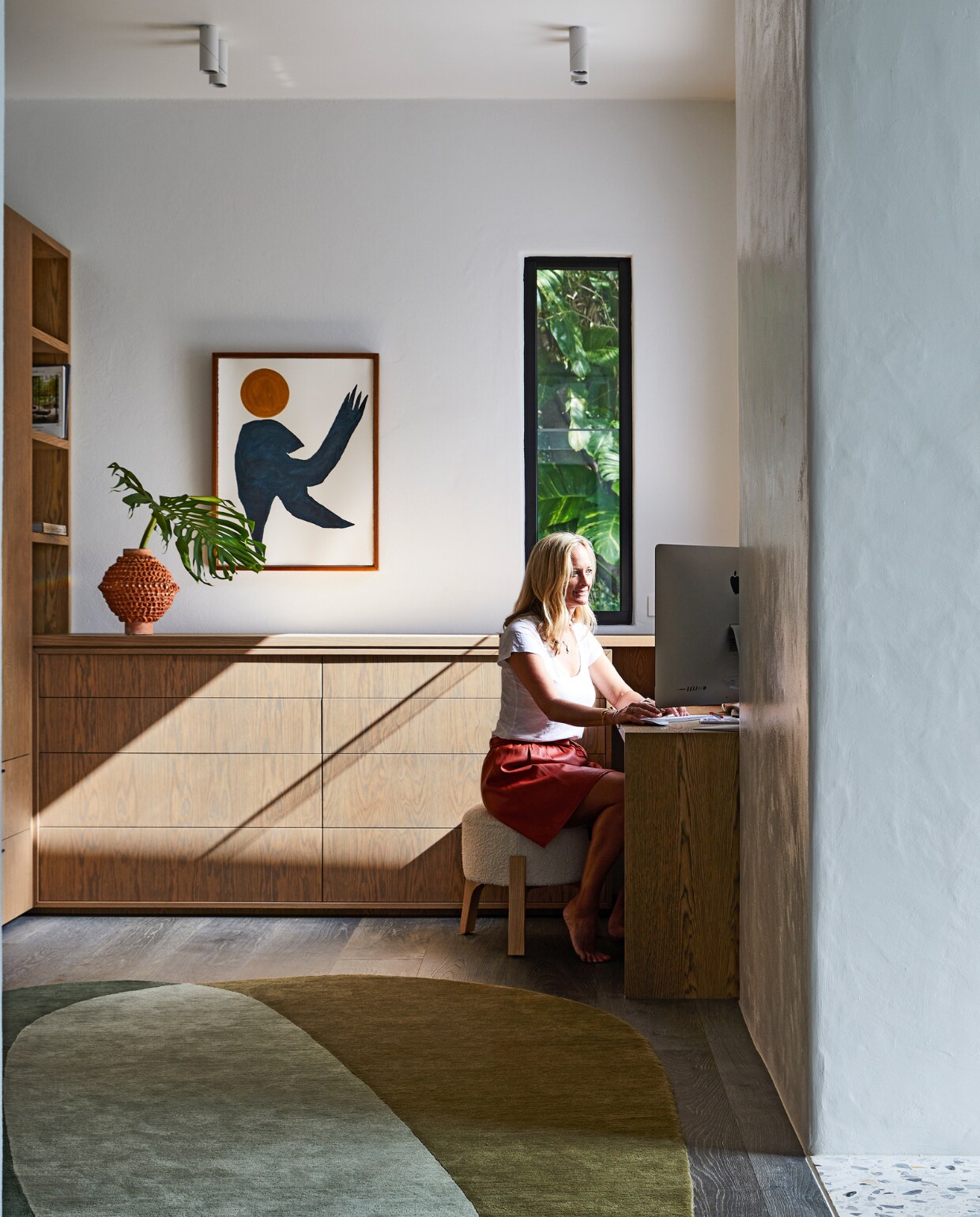 Studeerkamer met op maat ontworpen meubels van eikenhout. Kunstwerk Raven Sun van Hannah Nowlan. Kruk Castlery. Oranje vaas en vloerkleed Pebble Moss Jardan. vtwonen special binnenkijken 06-2022 | productie Living Inside | styling Julia Green | fotografie Armelle Habib