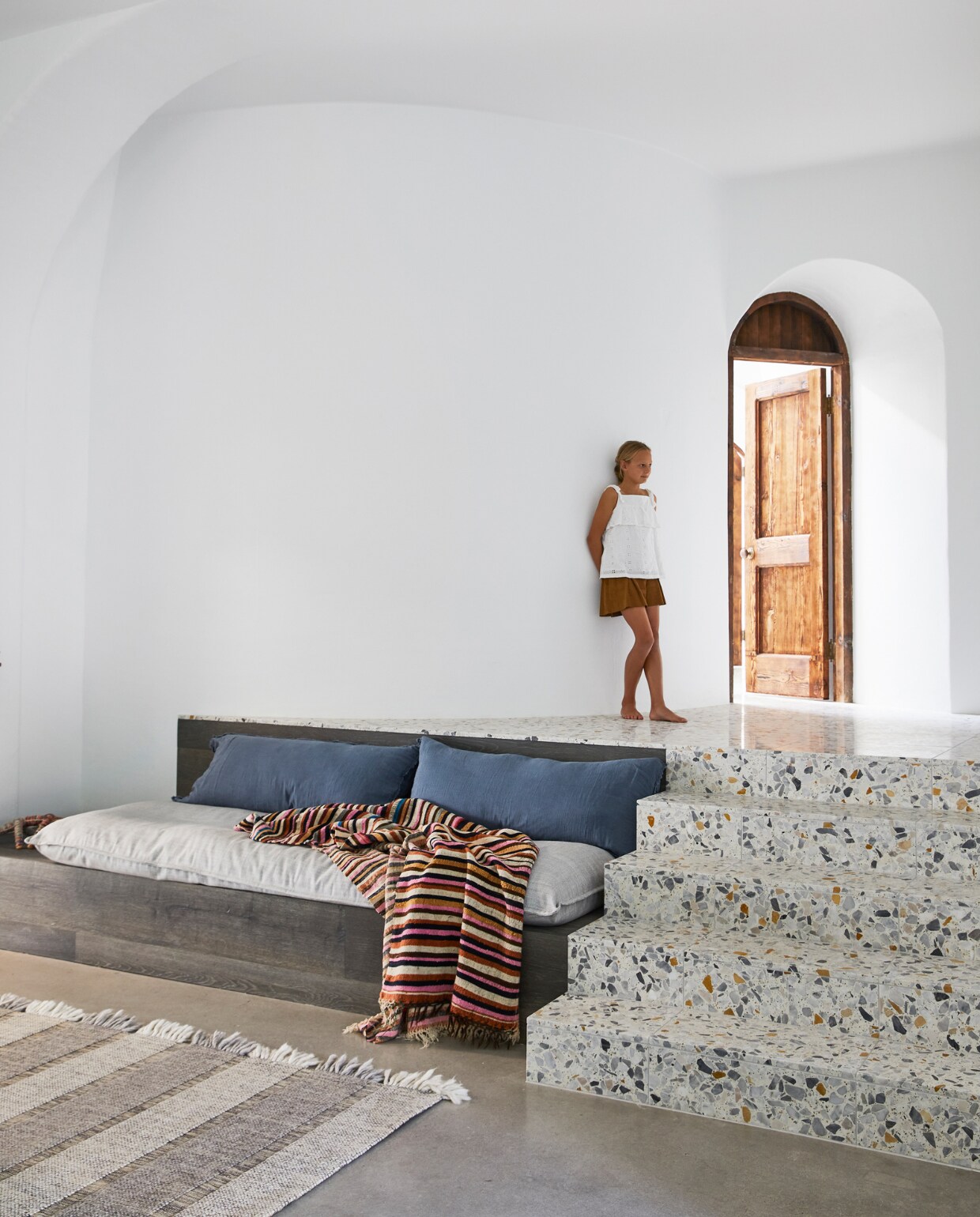 Mia in de speelkamer. Vloeren van gepolijst beton. Trappen van terrazzo tegels Ciottolo Grande van Ceramica Senio. Vloerkleed HC Monte Tribe Home. Op maat gemaakte zitbank Anchor &amp; Belle. Groot kussen Hale Mercantile Co., rugkussens op maat gemaakt. Deken Greenhouse Interiors. vtwonen special binnenkijken 06-2022 | productie Living Inside | styling Julia Green | fotografie Armelle Habib