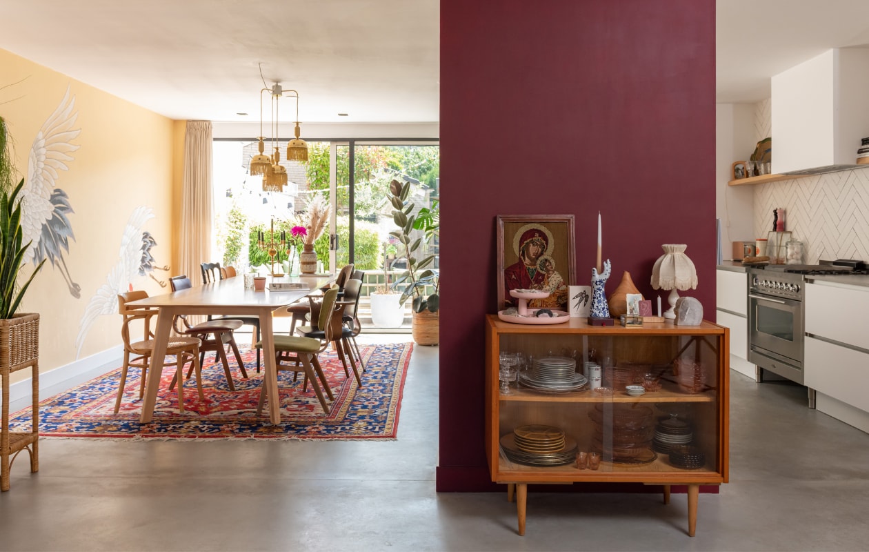 Behang Photowall. Verfkleur Power Chili van Vestingh. Vintage tapijt Meneer en Mevrouw de Boer. Eettafel Samt van De Machinekamer. Stoelen Vintage Friends en Loods 5. Franjelamp en vazen in het raam Sprinkelhop. Gouden kandelaar en religieus schilderij Bikkel Store. Houten vitrinekastje Vint. Servies en schemerlamp tweedehands. Roze etagère Vitra. Handkandelaar Polspotten. Overig onbekend. vtwonen special binnenkijken 03-2023 | styling Sharon Roest | fotografie Caroline Martinot