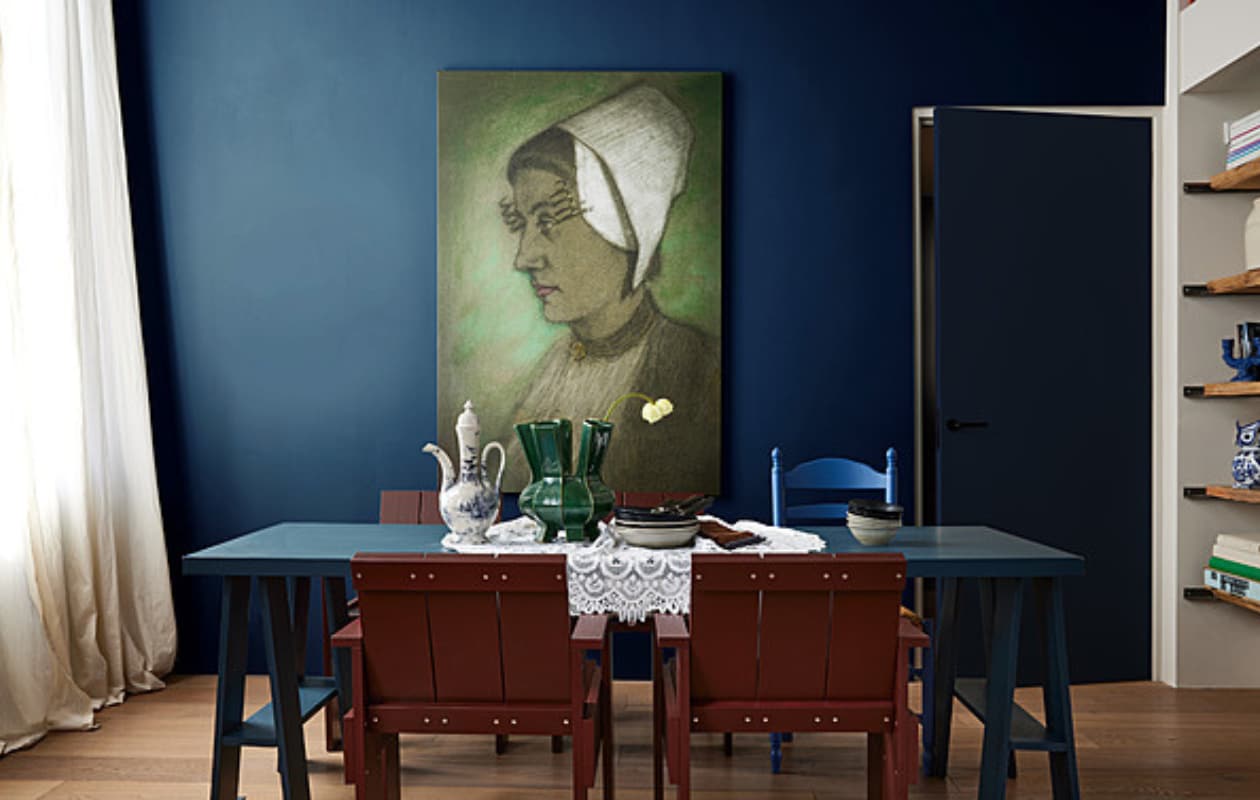 Muurverf en lakverf op deur Hague Blue van Farrow &amp; Ball (deruamsterdam.nl). Knopstoel Breugel, geverfd in ral 5014 (merkelbach.nl). Vurenhouten stoelen Krat gemaakt door Hay, 57,5x64x81 cm (bxdxh) (rietveldoriginals.com). Canvas reproductie Zeeuws meisje van Affect Fotografie, 115x170 cm (bxh) (werkaandemuur.nl). Keramieken vaas Puyi, 28,5x34 cm (Øxh), porseleinen spaarpot Owl Piggy (polspotten.nl). Tafel op schragen, 220x80 cm (lxb) prijs op aanvraag, kanten tafelkleed, antiek bestek (com-anders.nl). Keramieken kandelaar Dito van Ferm Living, 25x8x16 cm (bxdxh) (vtwonen.nl/shop). Keramische kan Cascade van Nordal (deens.nl). Borden Grainy, set van 4, kommen Grainy, servetten (nordal.eu). Overig privébezit. vtwonen 08-2023 | styling Marianne Luning | fotografie Alexander van berge