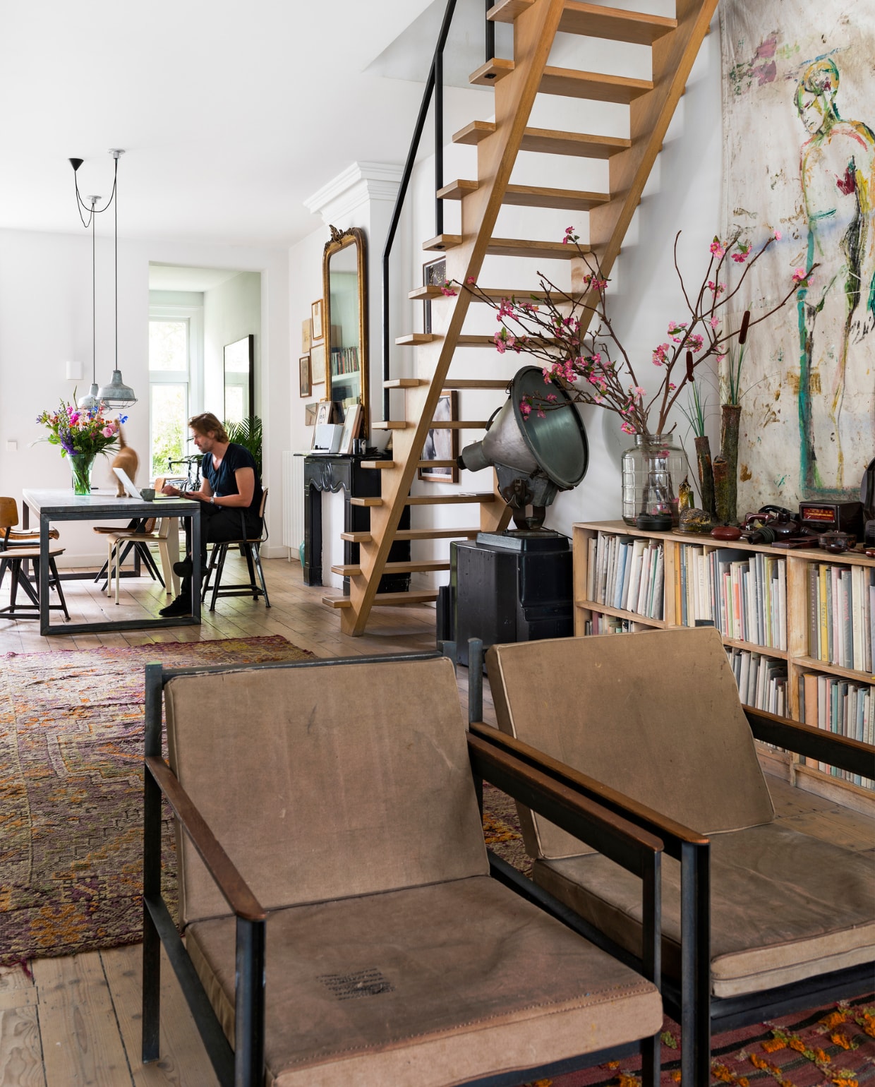 Fauteuils van Loftstyles in Antwerpen. Vloerkleed uit India, tafel uit Bali, lampen van een vintage markt. De kast voor alle kunstboeken is een eigen ontwerp en afgestemd op de maat van het grootste boek. Achter de kast een doek van Jasper. Onder de trap staat een stadionlamp op een mal van de Nederlandse Spoorwegen. Het hekwerk naast de trap is gemaakt door Fraai Metaal, een kunstenaar die met staal werkt. Hij heeft het staal gemoffeld, waardoor het een matte kleur zwart krijgt. vtwonen 10-2016 | fotografie Stan Koolen | styling Emmy van Dantzig