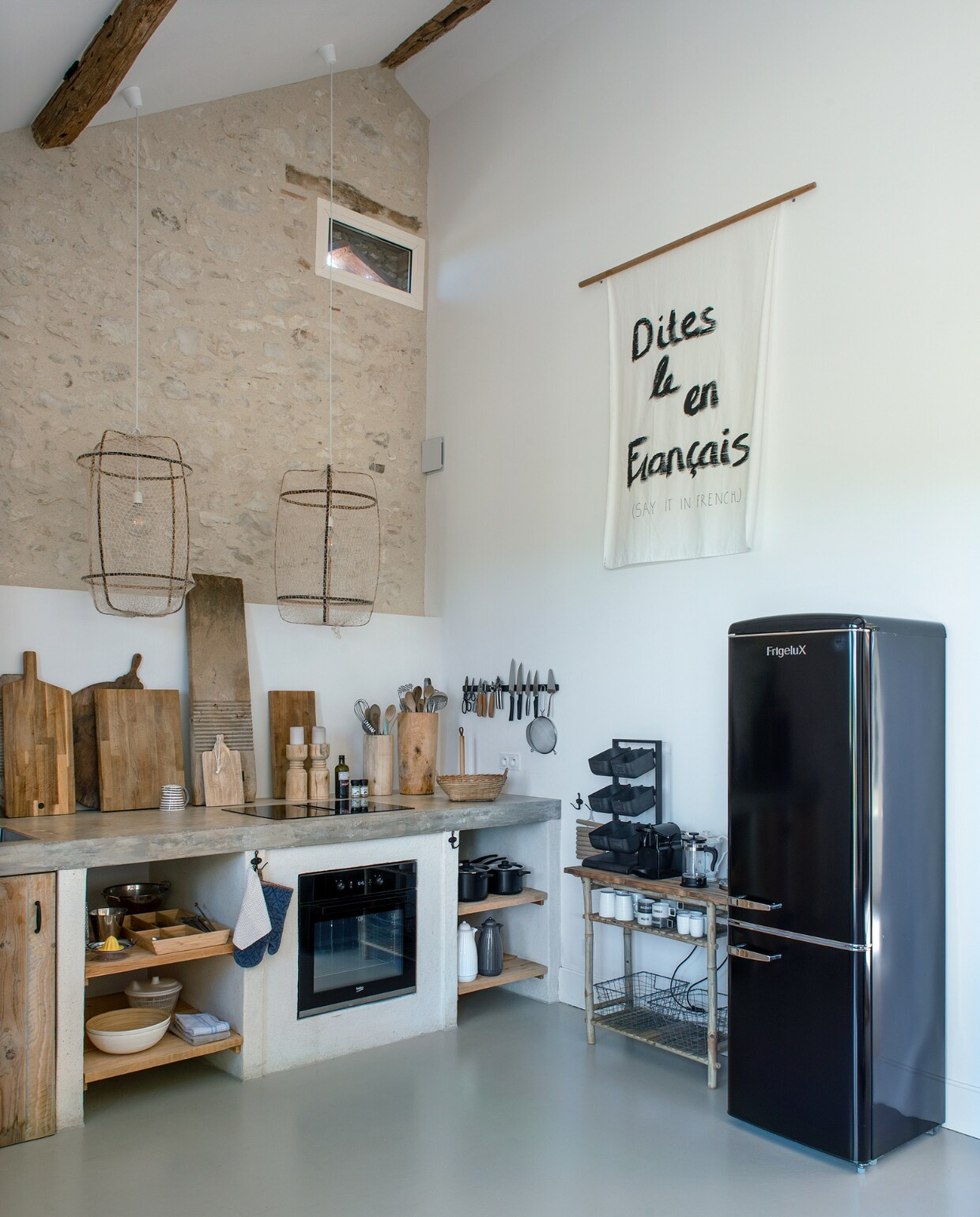 Keuken eigen ontwerp met betonnen blad en deuren van oud hout. Koelkast Darty. Hanglampen @just_bysan. Wanddoek @lhkphotoanddesign. Houten kandelaars Bloomingville. Houten potten en planken brocantewinkels. Mand Tine K Home. Zwart voorraadrek Chic Antique. Bekers Zusss en Maisons du Monde. Overig onder andere Ikea. vtwonen special binnenkijken 06-2023 | fotografie Ton Bouwer | productie Monique van der Pauw