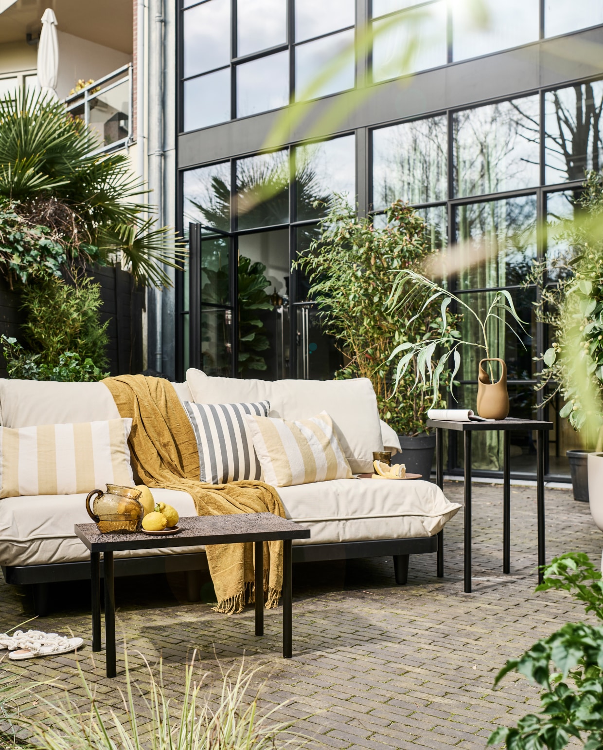 Modulaire loungeset Paletti van Fatboy, kunststof frame met waterafstotende kussens € 899,-, bruine stenen vaas Nicita van Bloomingville € 58,90 (vtwonen.be/shop). Plaid € 12,99, blauw gestreept kussen € 17,99, geel gestreept kussen € 17,99, glazen karaf € 29,99, houten onderzetter € 5,99, houten dienblad € 17,99, drinkglazen € 5,99 (zarahome.com). Overig privébezit. vtwonen 08-2023 | styling en uitvoering Sanne Ketelaar | fotografie Sjoerd Eickmans
