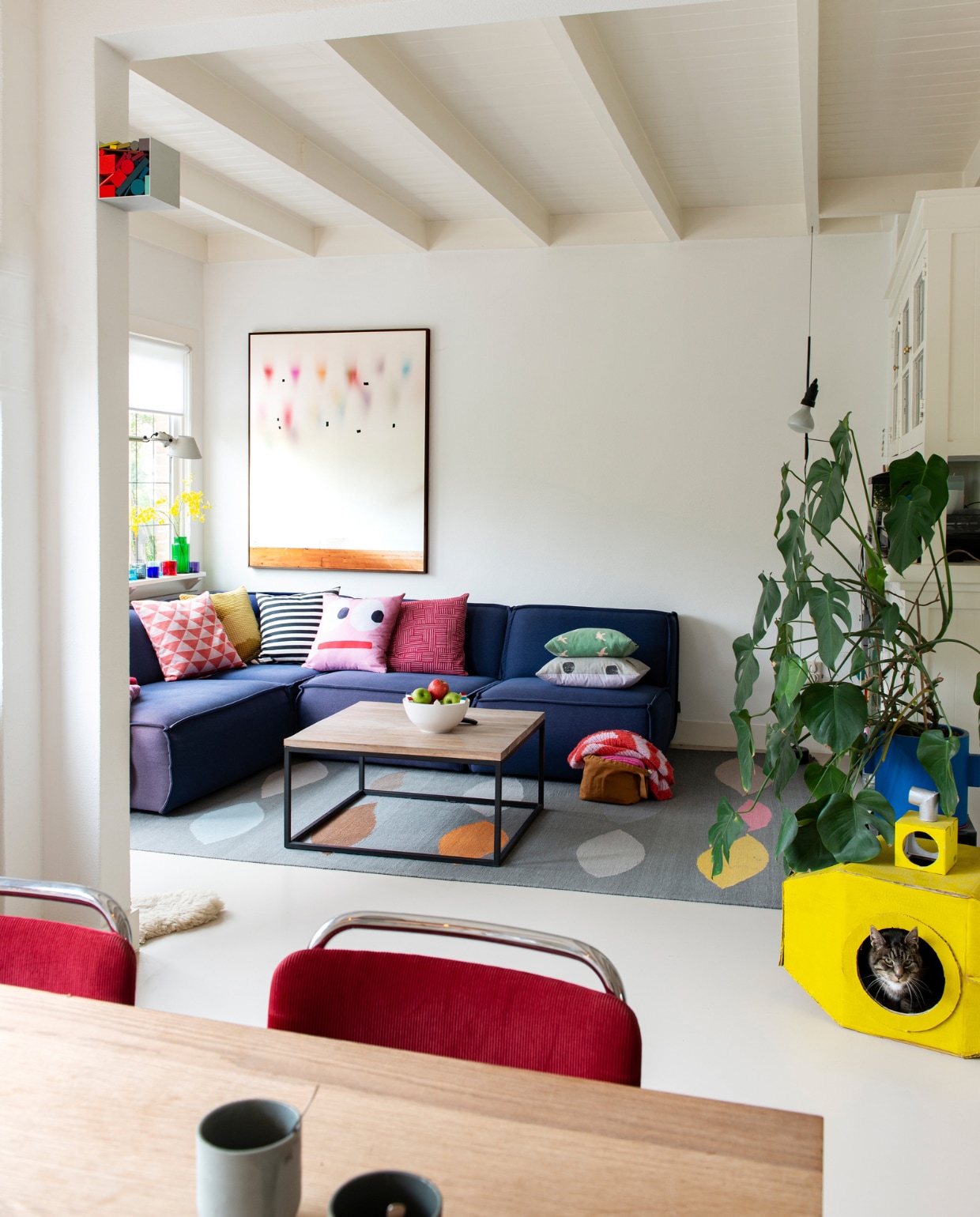 Kubus met kleuren van Sophie Smallhorn. Op vensterbank: lamp Tolomeo van Artemide, theelichten Iittala. Bank Edge van Fest Amsterdam, kussens van diverse herkomst, fotografisch kunstwerk van Katja Mater via Galerie Heden, salontafel laten maken door smid, schaal Bebouwde Kom van Olav Slingerland, karpet Leaves van CarpetVista, in de hoek lamp Parentesi van Flos, blauwe bloempot Serax, stoelen model 101 van Gispen, op maat gemaakte eettafel Jacco Bakker, mokken De Intuïtiefabriek. vtwonen 07-2021 | styling Jeske Weel | fotografie Caroline Coehorst
