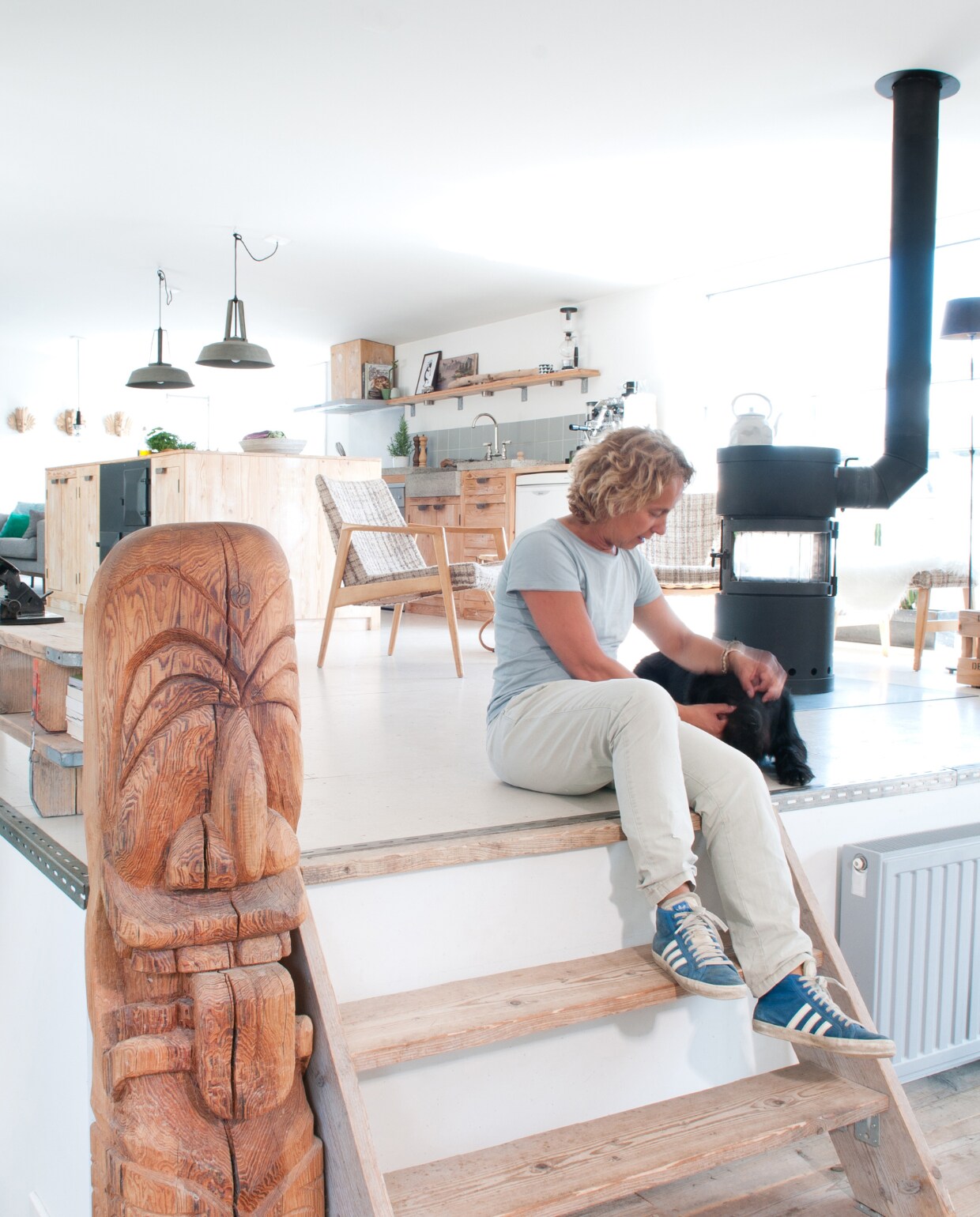 Op de vloer in de eethoek liggen steigerhouten planken. De radiator rechts van het trappetje is nieuw, maar – net als alle andere radiatoren – industrieel gemaakt met de leiding aan de buitenkant, een metalen knop en grijze verf. Lampen Nijhof, kachel via Marktplaats, werkeiland gemaakt van oude kaasplanken. Fauteuils kringloopwinkel. vtwonen 03-2017 | styling Irene van den Brink | fotografie Suzanne Paap