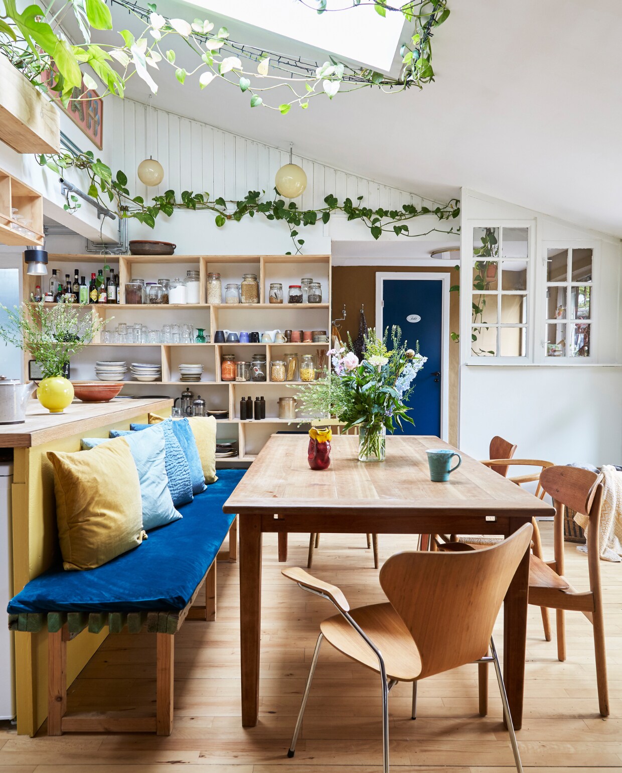 Kersenhouten eettafel uit vorig huis. Vintage vlinderstoelen Arne Jacobsen, stoelen CH30 en stoel CH24 van Hans Wegner. Kussens Ikea. Glazen bollen rommelmarkt. Bank, matraskussen en keukenkast zelfgemaakt. Serviesgoed, glaswerk en keramiek rommelmarkten en lokale pottenbakkers. vtwonen special binnenkijken 06-2023 | productie Living Inside | fotografie Anitta Behrendt | styling Rikke Graff Juel