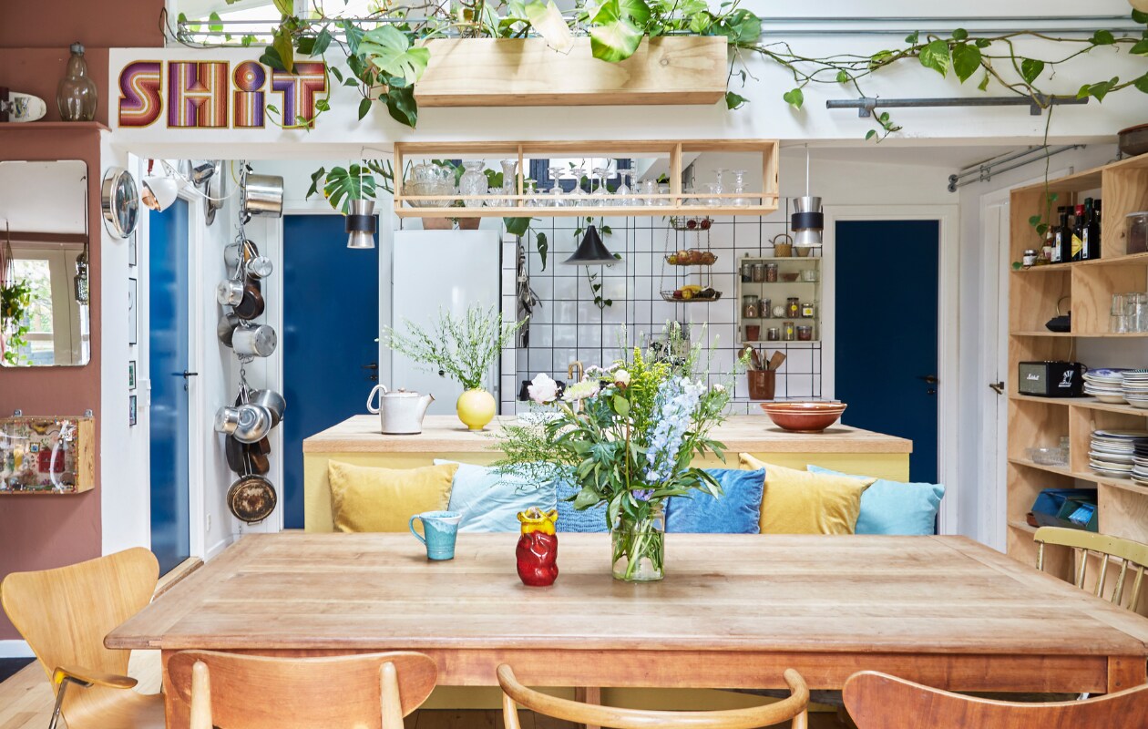 Kersenhouten eettafel uit vorig huis. Vintage vlinderstoel Arne Jacobsen, stoelen CH30 en stoel CH24 van Hans Wegner. Kussens en metalen rek Ikea. Keukenkast zelfgemaakt. Serviesgoed, glaswerk, spiegel en keramiek rommelmarkten en lokale pottenbakkers. Aardewerk op tafel uit Griekenland. Zwarte hanglamp rommelmarkt. De letters zijn puzzels van Maduro. Bluetooth-speaker Marshall. Hanglampen boven kookeiland vlooienmarkt. Overig vintage, zelfgemaakt of onbekend. vtwonen special binnenkijken 06-2023 | productie Living Inside | fotografie Anitta Behrendt | styling Rikke Graff Juel