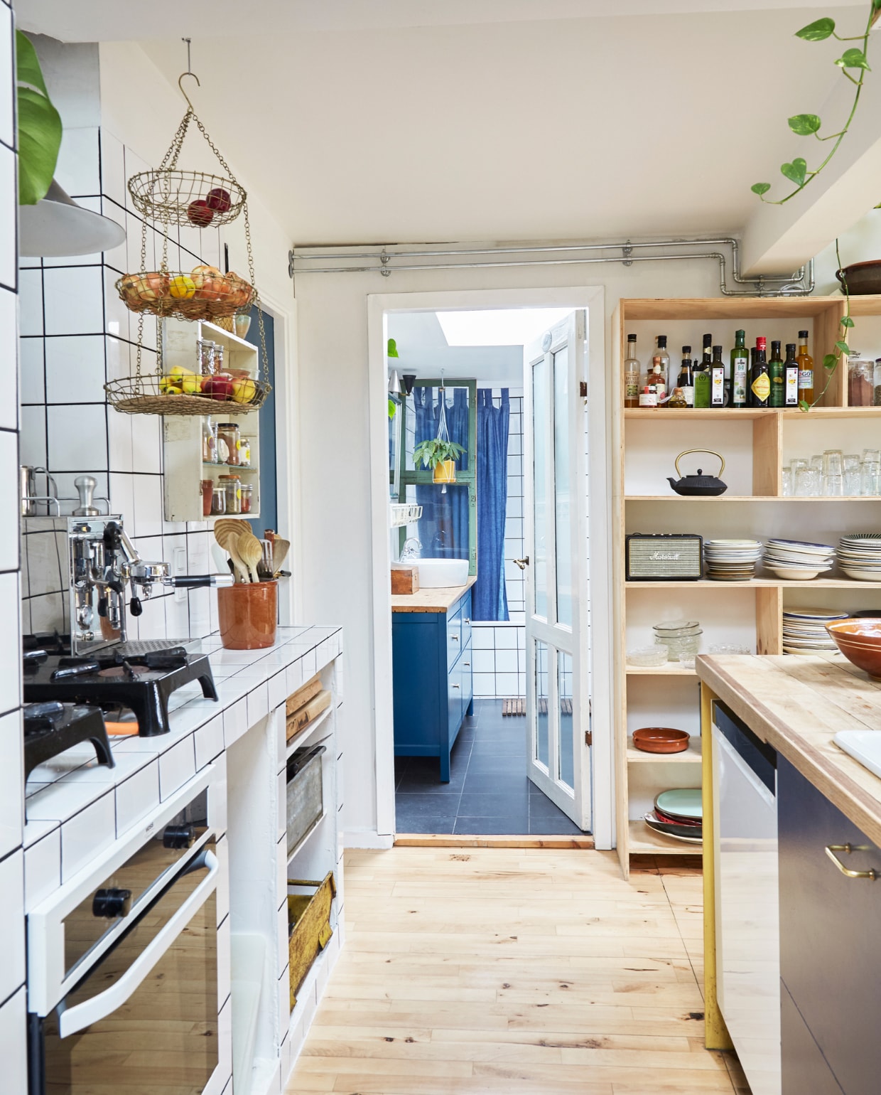 Keuken en wandkast zelfontworpen en -gemaakt. Wandkastje met glazen planken tweedehands. Metalen bakken onder aanrecht, serviesgoed, glaswerk en keramiek rommelmarkt en lokale winkels. Metalen hangmand Notre Dame. vtwonen special binnenkijken 06-2023 | productie Living Inside | fotografie Anitta Behrendt | styling Rikke Graff Juel