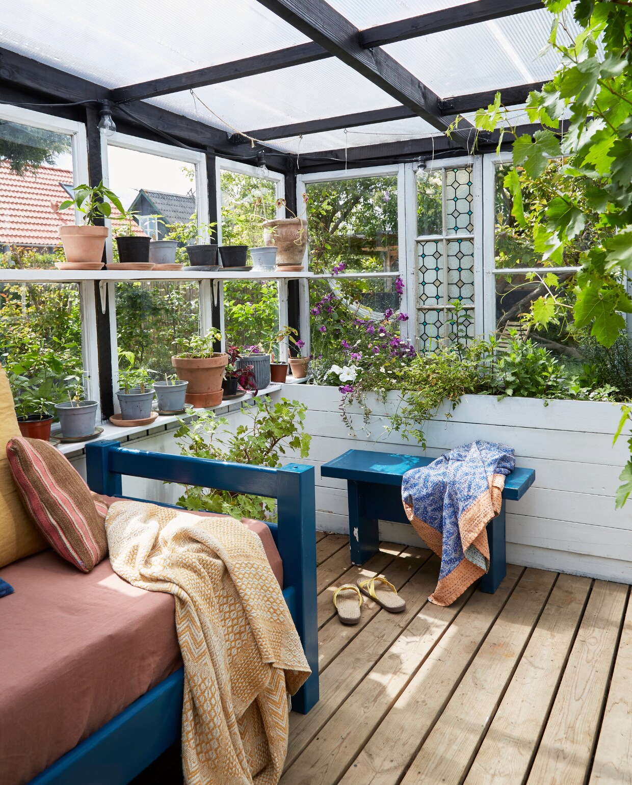 Serre gebouwd van oude ramen. Kussens Smukt Brugt, Ikea en uit Marokko. Gele plaid Netto. Blauwe plaid van kerstmarkt in Fuglebjerggaard. Daybed en bankje zelfgemaakt. vtwonen special binnenkijken 06-2023 | productie Living Inside | fotografie Anitta Behrendt | styling Rikke Graff Juel