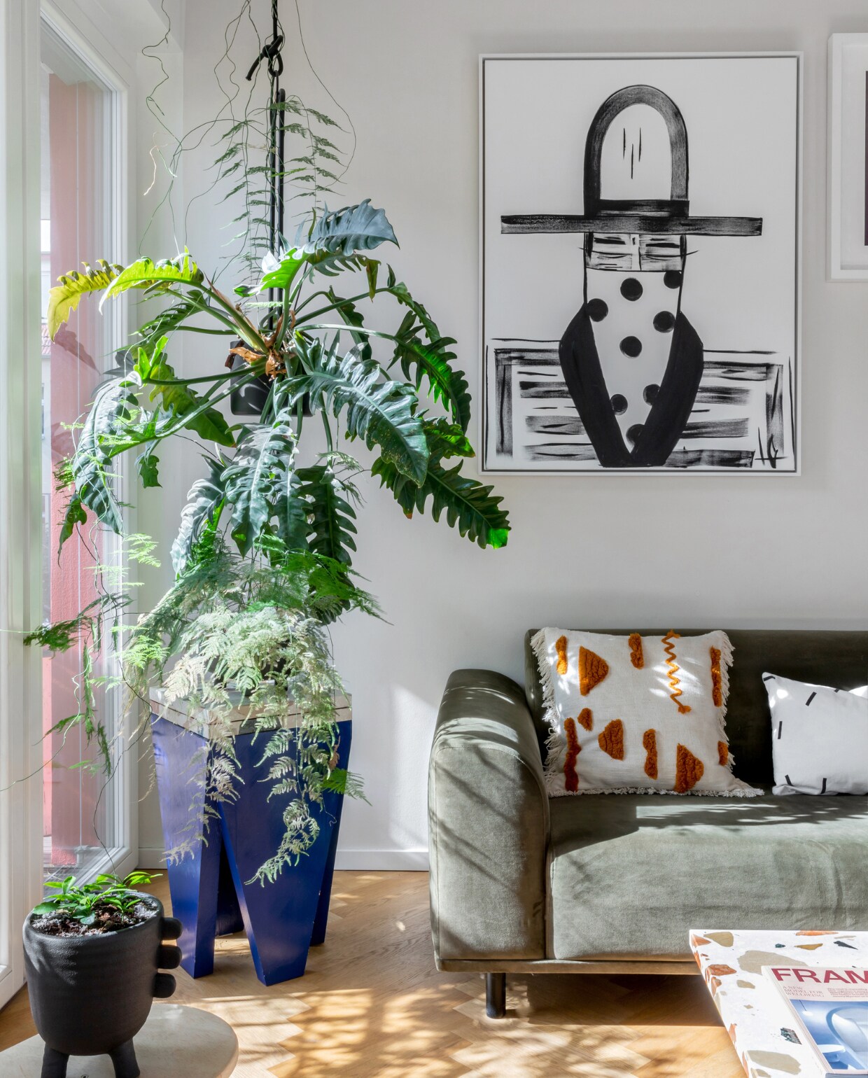 Bank Hannah van Bolia. Plantenpot en zwart-wit kussen Ferm Living. Oranje-wit kussen The Masie. Bijzettafel Studio Elliot White. Kunstwerk Cowboy van Laura Goodson Art. Overig onbekend. vtwonen special binnenkijken 06-2023 | productie &amp; fotografie Anne-Catherine Scoffoni | styling Raini Peters