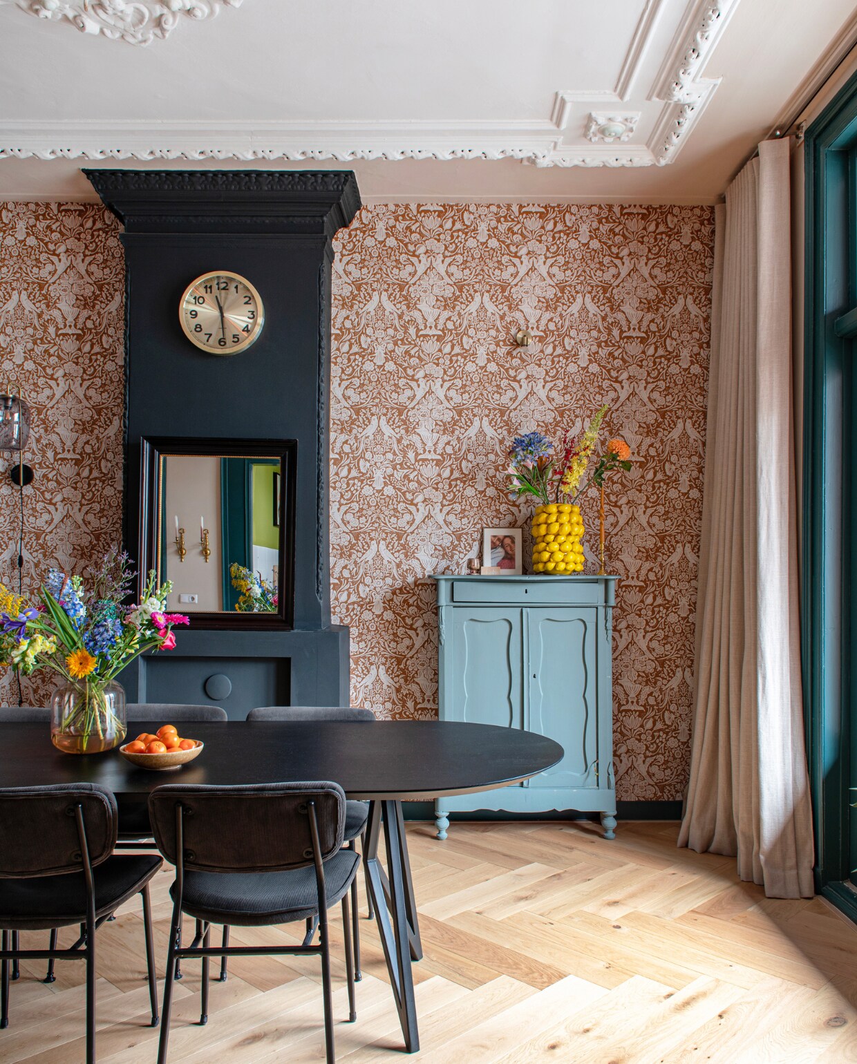 Behang en gordijnen Karwei, klok Karlsson, eettafel Studio Henk, stoelen Wonenmetlef, vaas Des Pots, vintage kast geschilderd in Livid van Little Greene, wandlamp Marktplaats. Muurverf schouw Off-Black van Farrow &amp; Ball, muurverf plafond IG KH M-058 van Karwei. Visgraatparket Blank Geolied Eiken van vtwonen via Karwei. Overig onbekend. vtwonen 09-2023 | productie De Binnenkijkers | styling Jeske Weel | fotografie Caroline Coehorst