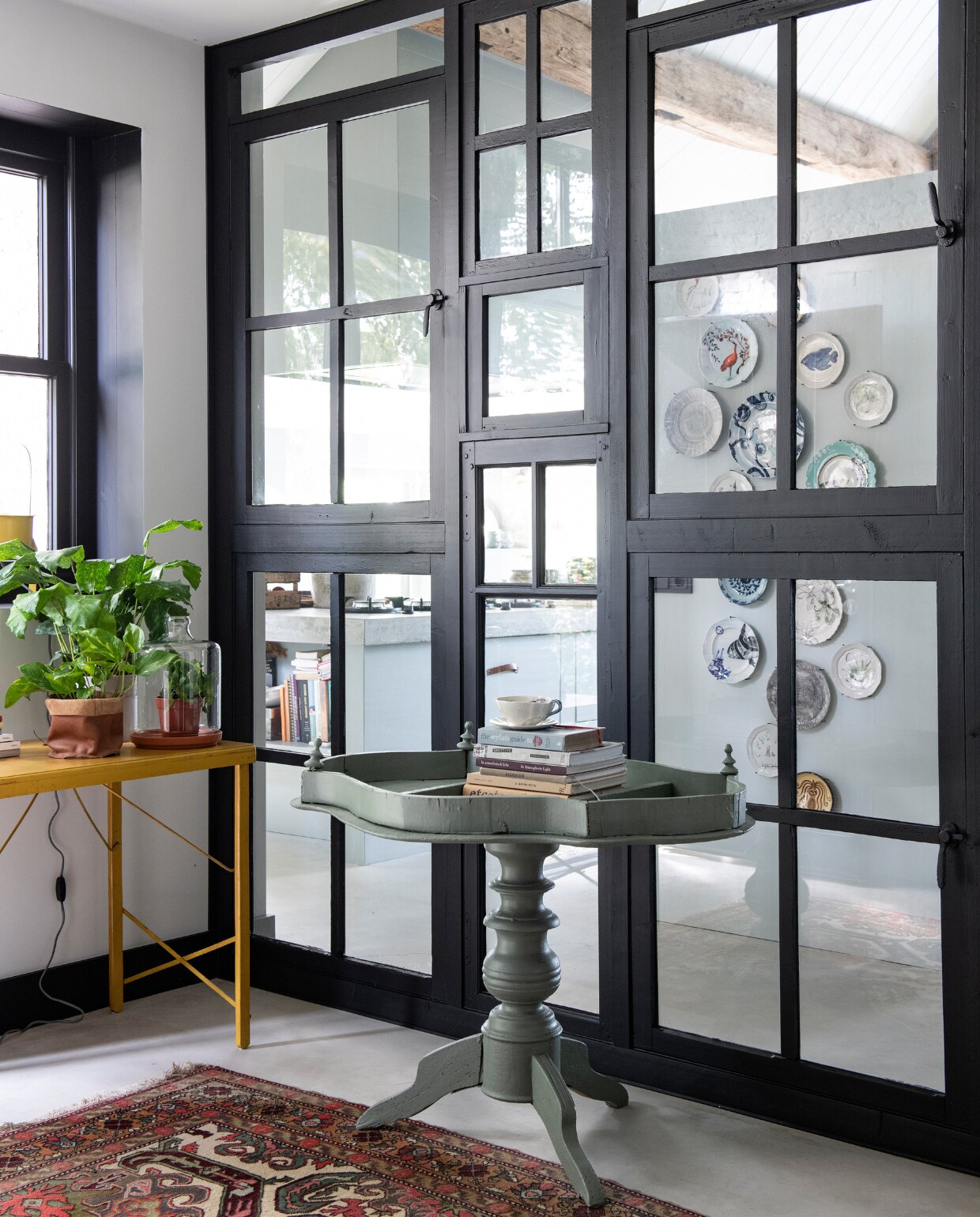 De hergebruikte raampartijen zijn geschilderd in kleur Ash van Stapelgoed. De bordencollectie is een herinnering aan vakanties en bijzondere gelegenheden. Leren opbergzak op de plantentafel Stapelgoed, vloerkleed en bijzettafel zijn vintage stukken. vtwonen 11-2019 | styling Esther Loonstijn | fotografie Louis Lemaire