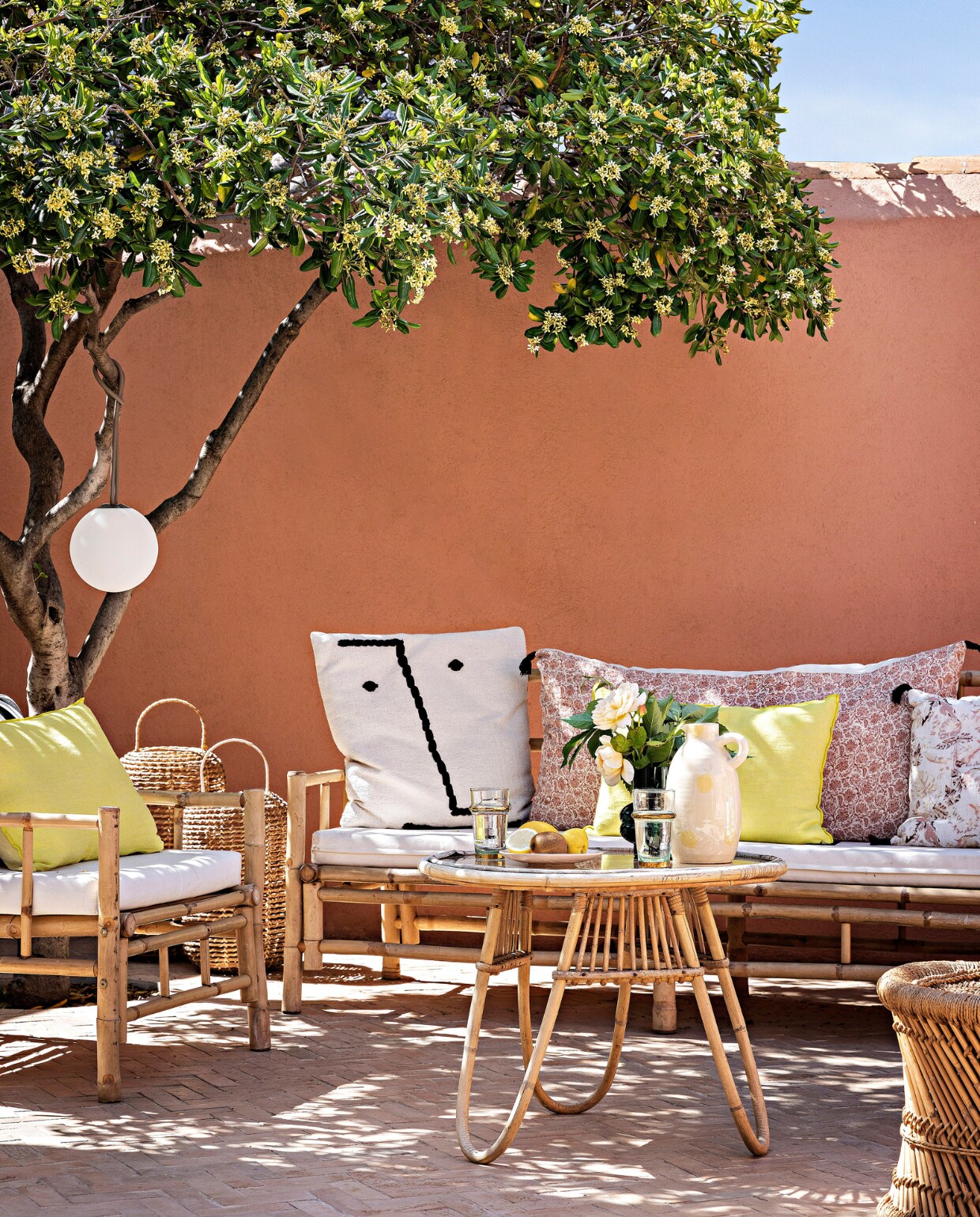 Ambachtelijke bejmattegels Art et Sud. Muren geschilderd met leemverf Terre Rose van Ressource. Bank en fauteuil Decoclico. Zitkussens Ambiance et Matières, kussen zwarte streep Maison Madeleine, gele kussens Maison de Vacances, bloemenkussens Cyrillus. Rotan tafel erfstuk. Gele kan Oustao. Hanglamp Fatboy. Rotan lantaarns en Marokkaanse kruk Jiji La Palme d’Or. vtwonen special binnenkijken 06-2023 | productie &amp; styling Marie Maud Levron | fotografie Yann Deret