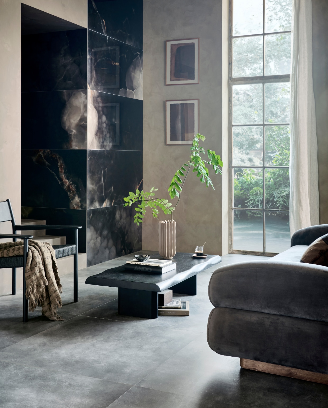 Op de wand: tegels Onyx Deep Dark, 60x120 cm, per m² € 92,50. Op de vloer tegels Mold Basalt, 90x90 cm, per m²  € 89,50.M.m.v. pand-40.nl (bank van Nordal), pure-original.com (muurverf Artisan Tan, verf op de trap Cold Lava), basiclabel.nl (fauteuil Lael van Woood, salontafel Cali van Woood), mooswillemsen.com (kunstwerken), zarahome.com (plaid, linnen gordijn, houten doos met metalen deksel, houten onderzetter), hm.com (vaas). Overig privébezit. vtwonen 09-2023 | productie Tanja Saarberg | styling Sanne Ketelaar | fotografie Sjoerd Eickmans