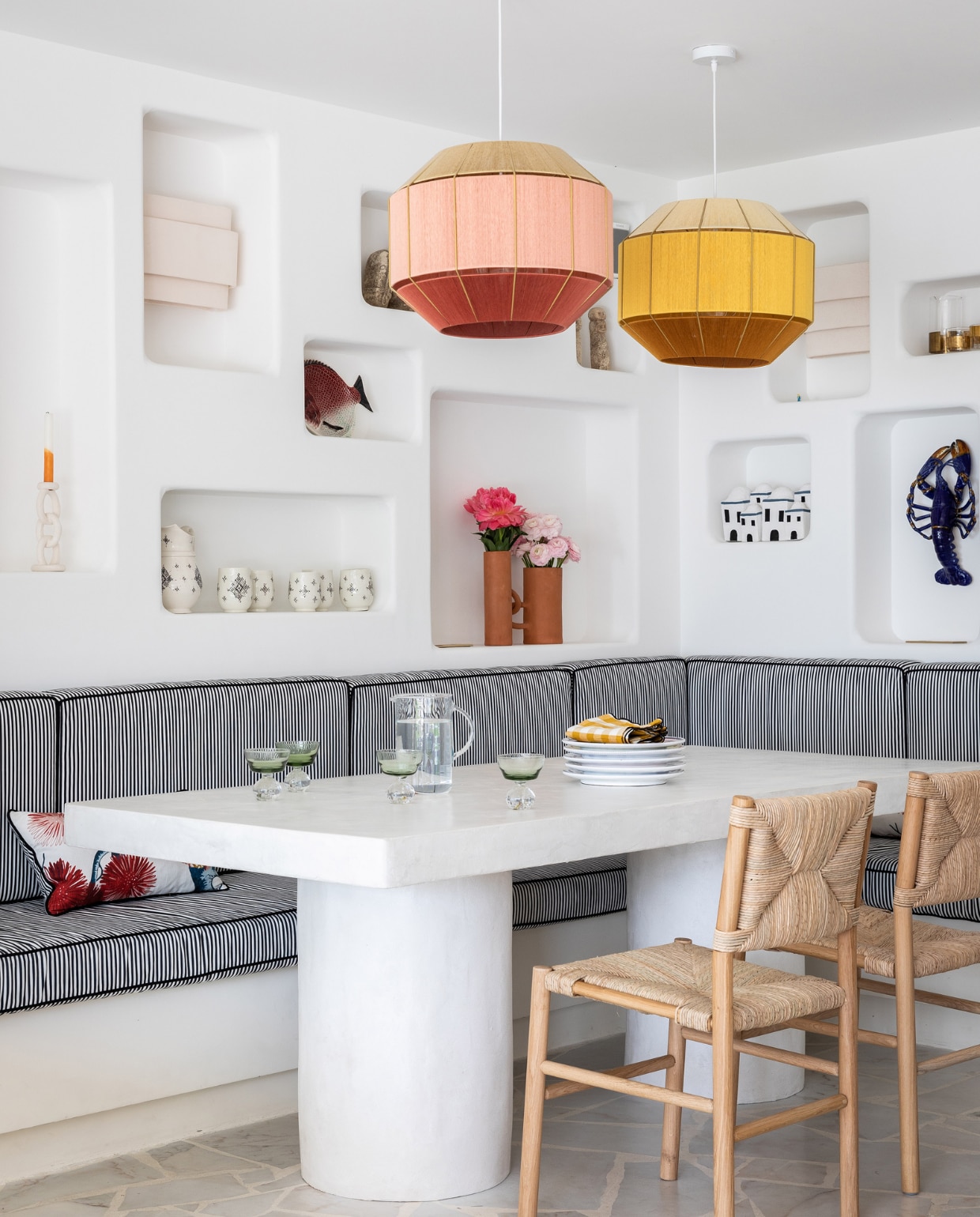 Vloer gemaakt van Portugees Estremoz marmer. Tafel ontworpen door Stéphanie, gemaakt door Laurence de Konrad. Zwart-witte bankkussens lokaal gemaakt. Hanglampen Julie Lansom. Stoelen Cadieras van Midi. Witte kandelaar en aardenwerken vazen Franca Atelier. Witte wandlampen in nissen en groene wijnglazen Serax. Huisjes souvenir. Kreeft Aussih. Overig onbekend. vtwonen 07-2023 | productie &amp; styling Marie Maud Levron | fotografie Yann Deret