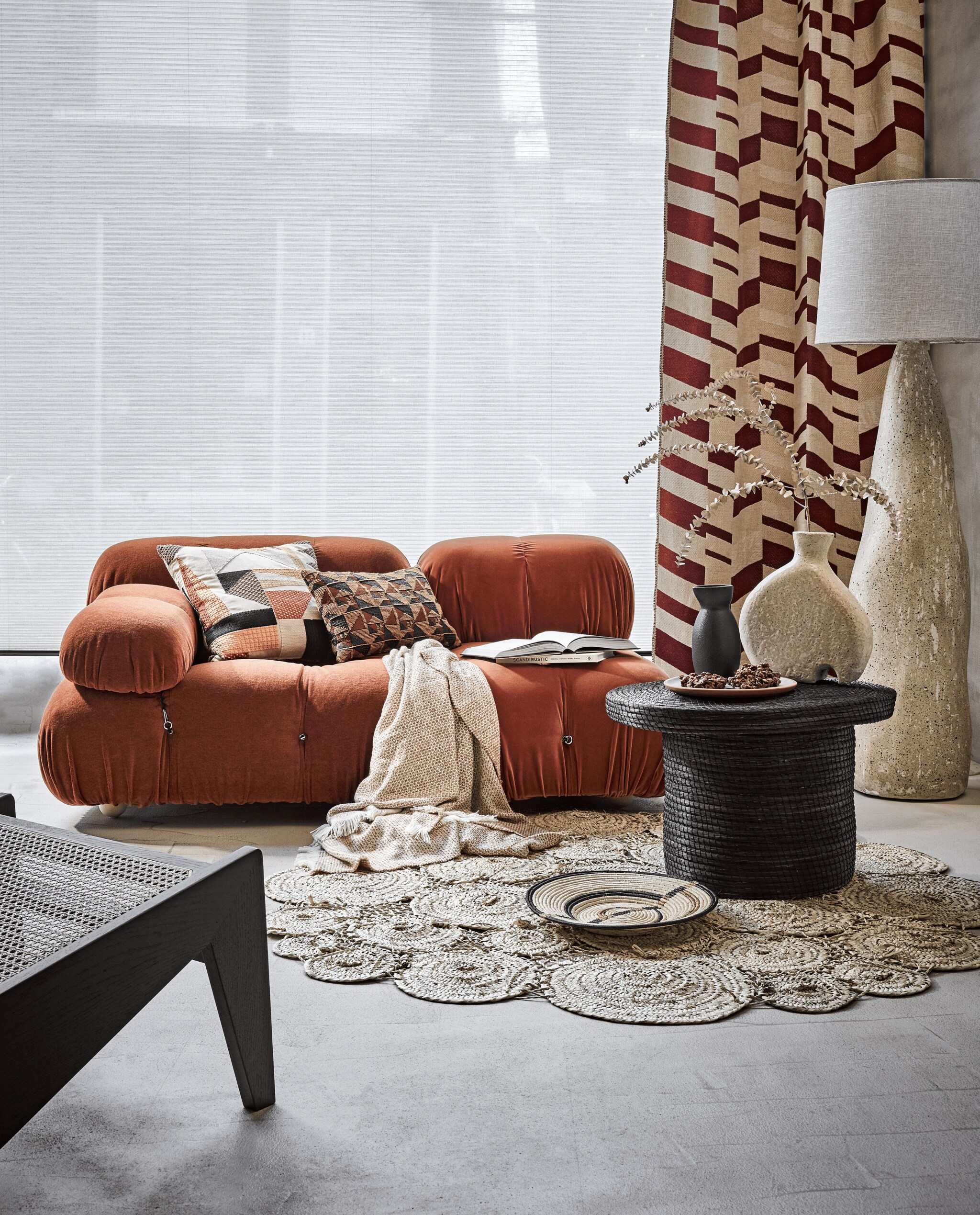 Beige licht doorlatende duettes van Style by Abz, per m² vanaf € 340,- (de-stoffeerder.nl). Gordijn van stof Rif van Nobilis, mix van katoen, viscose, wol, linnen, modal en polyamide, 136 cm breed, per meter € 139,- (wva.nl). Bank Orange bestaat uit twee delen, prijs op aanvraag, loungestoel prijs op aanvraag (edha-interieur.nl). Kussen links van stof La 86935 van Elitis, per meter € 245, klein kussen van stof Lr 33122 van Elitis, per meter € 245 (loggerewilpower.com). Plaid, 140x190 cm € 45,99, zwarte kan, 10x20 cm € 22,99 (zarahome.com). Boek Scandi Rustic van Rebecca Lawson € 24,99 (hm.com). Kleed, ook te gebruiken als wandkleed, 150 cm € 330,- geweven schaal small op grond € 73, gevlochten tafel  € 275 (couleurlocale.eu). Lamp maat L € 699,95, beige vaas € 89,95, terra bord met groene binnenkant € 16,95 (lanena-home.com). Droogbloemen (plantje.nl). vtwonen 03-2022 | styling Liza Wassenaar | fotografie Alexander van Berge
