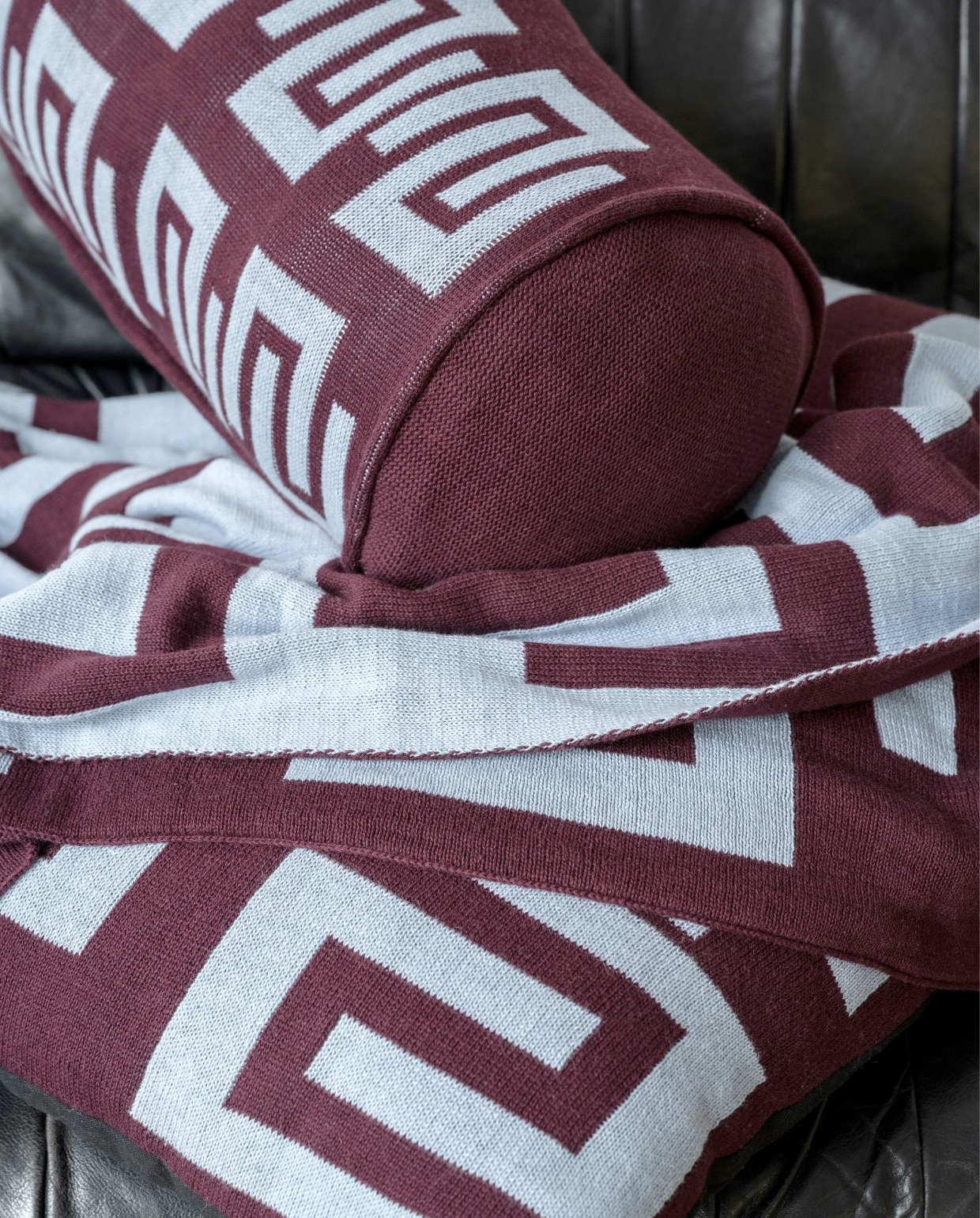 Bordeaux-lichtblauw rond kussen, gebreid bci-katoen, 20x50 cm € 49,95, bordeaux-lichtblauwe plaid met verschillend dessin aan beide kanten, gebreid bci-katoen, 130x170 cm € 99,95. vtwonen 10-2023 | productie en styling Tanja Saarberg | fotografie Stan Koolen