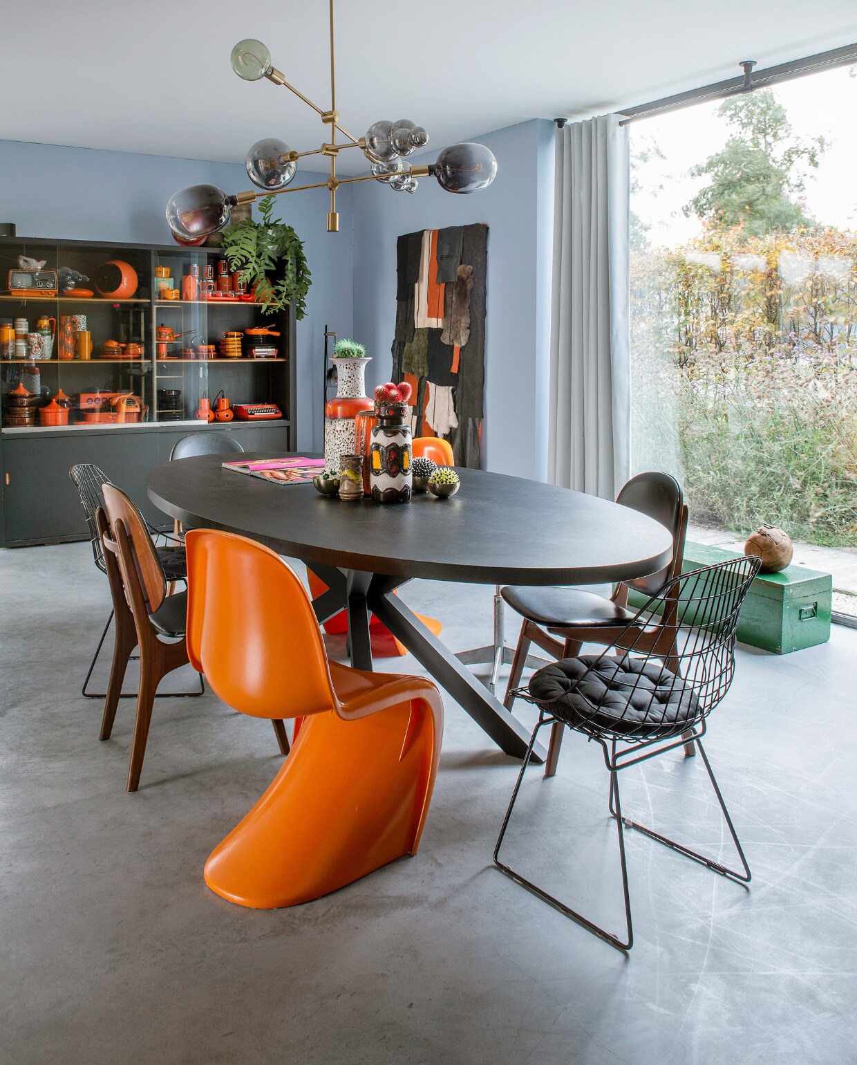 Vintage schoolkast zwart geverfd. Kunstwerk door Cor gemaakt. Houten eettafelstoelen geërfd van René’s grootouders. Oranje stoelen Verner Panton en draadstoelen Pastoe vintage. Wandkleur Bright Skies van Flexa. Overig onbekend of vintage. vtwonen 10-2023 | fotografie Ton Bouwer