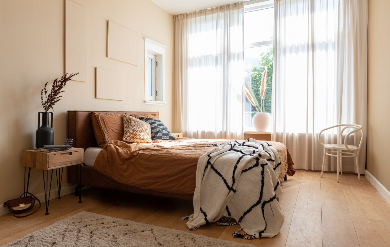 Muurkleur Medina van Histor, gordijnen Ikea. Nachtkastje, vloerkleed en bed Wehkamp Home. Vaas HKliving, glas Polspotten, tas Cotton Club. Beddengoed H&amp;M Home, sprei en kussens Karwei. Vazen Fést Amsterdam, pampaspluimen Kwantum, stoel kringloopwinkel. vtwonen 02-2023 | styling Sharon Roest | fotografie Caroline Martinot
