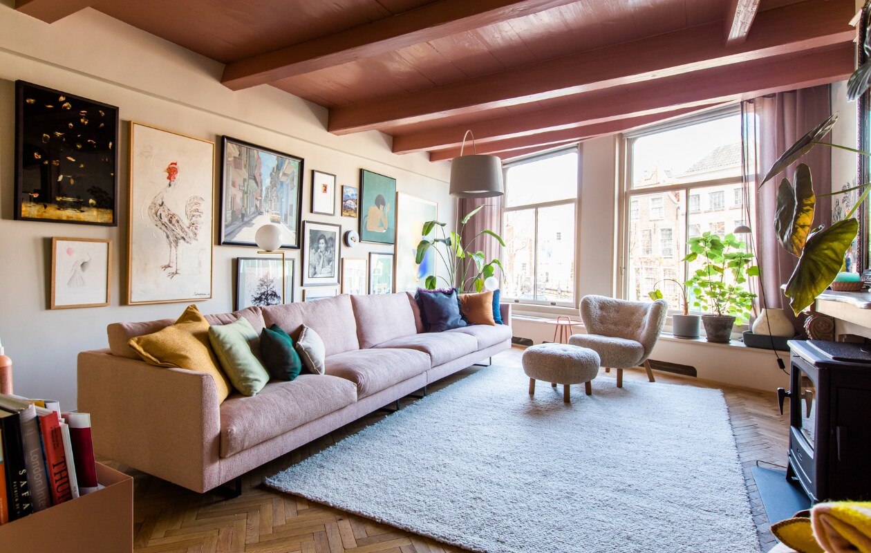 Bank en bijzettafel Montis. Kussens Hay, vloerkleed Ferm Living, visgraatvloer Het Leidsch Parkethuis. Verf plafond Blush van Little Greene. Bloempotten, fauteuil en poef &amp;Tradition. Booglamp Foscarini, gordijnen Femkeido, kachel Dover. Kunstwerken (v.l.n.r.): Titus Brein, kip uit Bali, Cuba van Lorenzo de Bruin, zwartwit-foto uit Honfleur, klein rood werk uit Zuid-Afrika, groot werk Isabelle Wenzel. Overig onbekend. vtwonen 10-2023 | productie CocoFeatures | fotografie Laura Emma van Geest